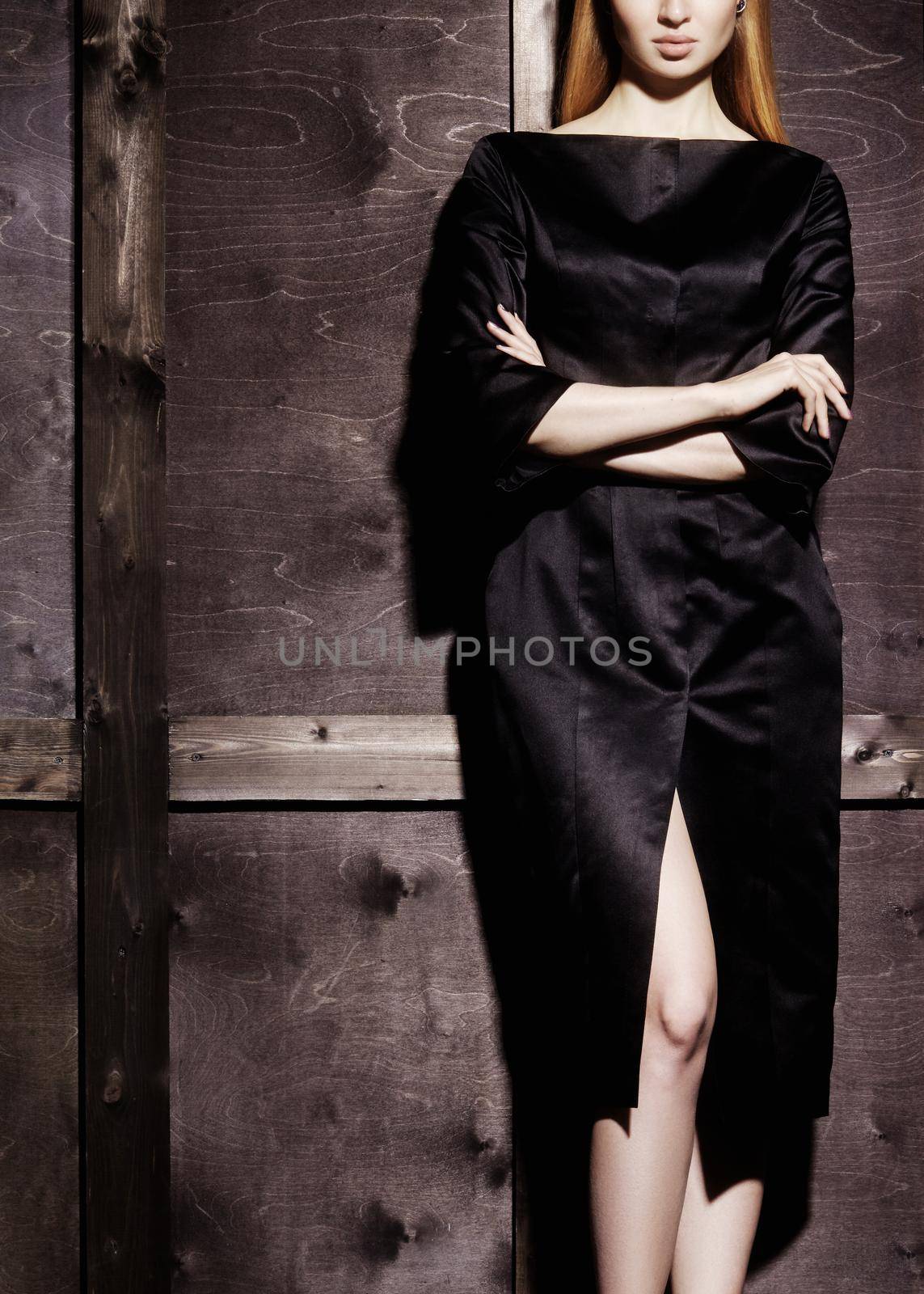 Fashion portrait of beautiful young woman in sexy black dress near with wood wall. Elegant dark evening look. Pretty lady with blond straight hair. Glamour style for luxury life