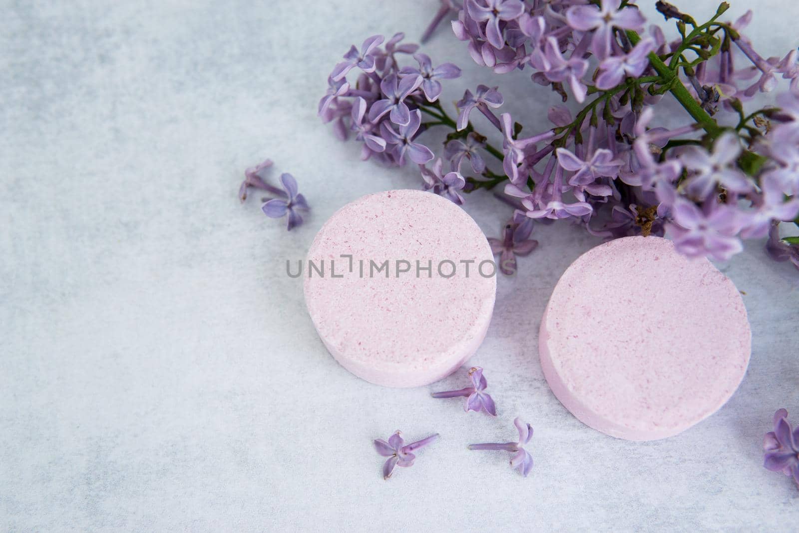 Concept of Spa-cosmetic and cosmetic procedures. Bath salt in effervescent tablets with lilac flowers on light concrete background. Concept of zero waste lifestyle. Space for text.