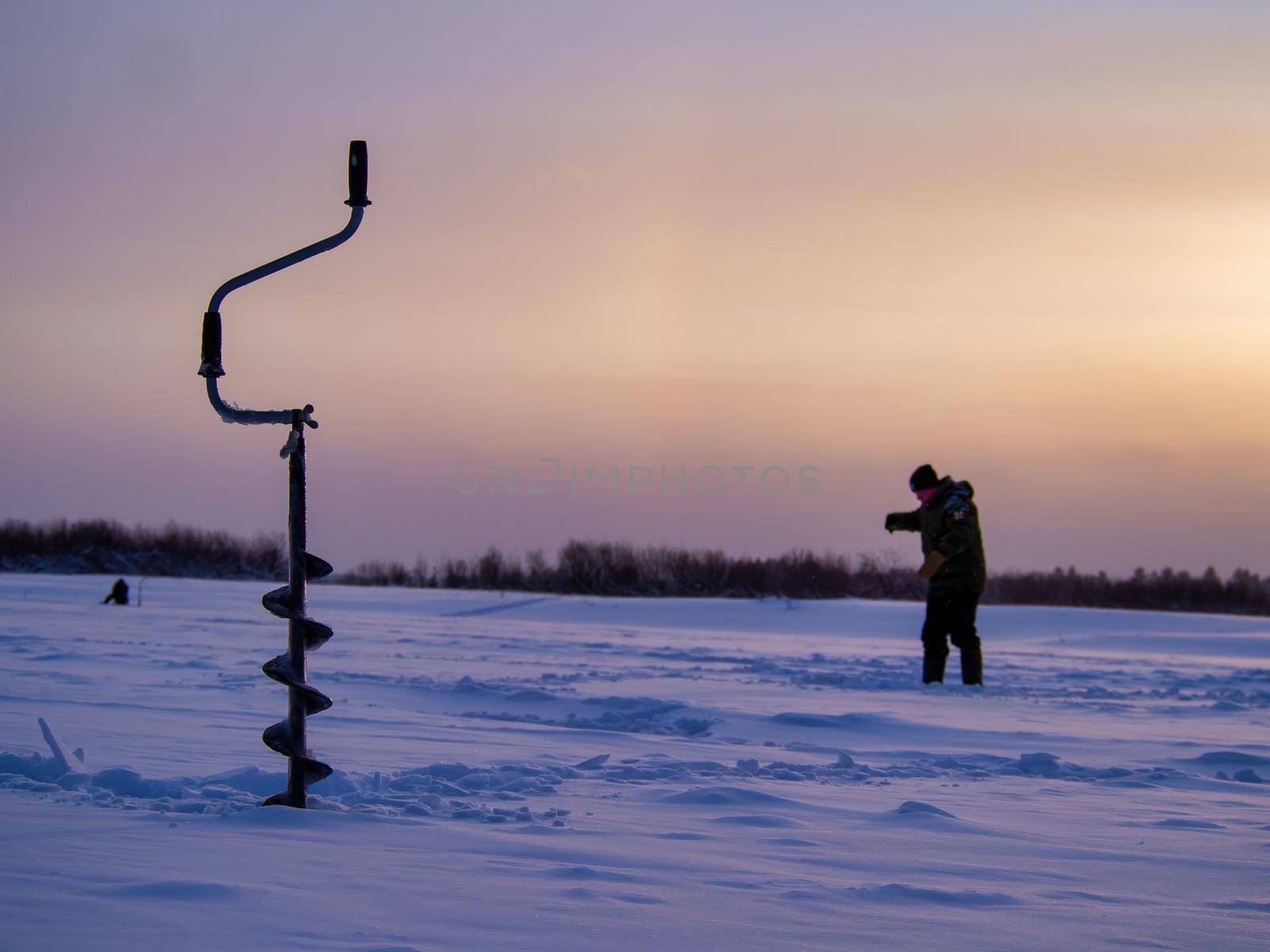 Ice drill on a frozen lake with a fisherman in the background