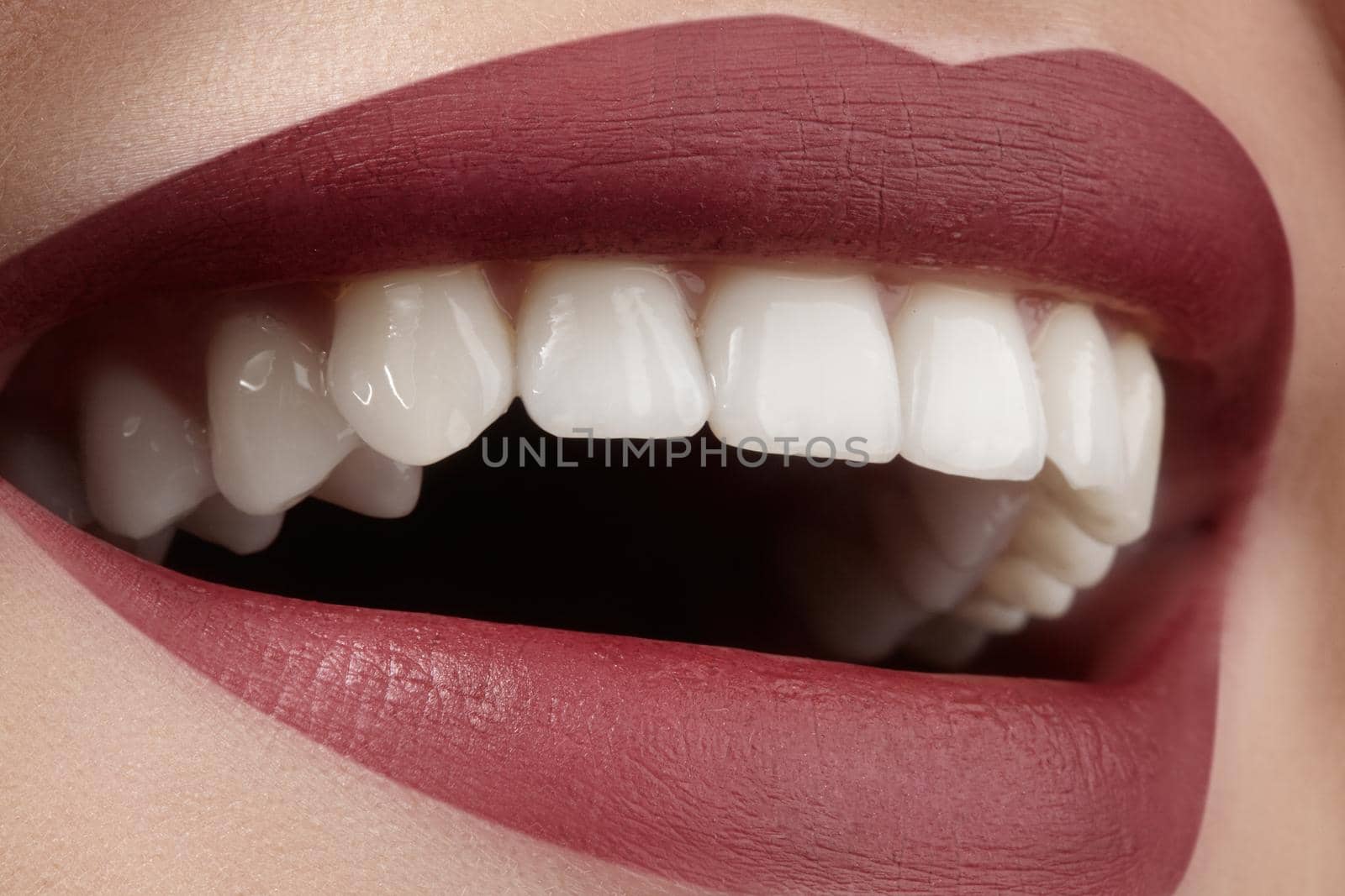 Wide smile of young beautiful woman with perfect healthy white teeth on grey background. Dental whitening, ortodont, care tooth and wellness. Red lipstick makeup on female lips.