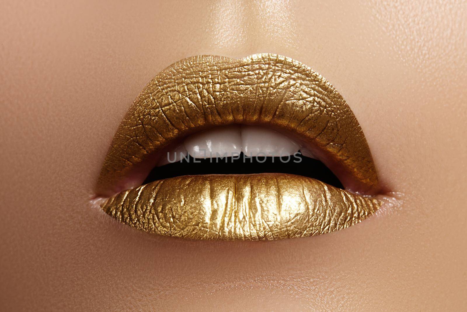 Beautiful closeup with female plump lips with gold color makeup. Fashion celebrate make-up, glitter cosmetic. Shine christmas style. Metalic makeup