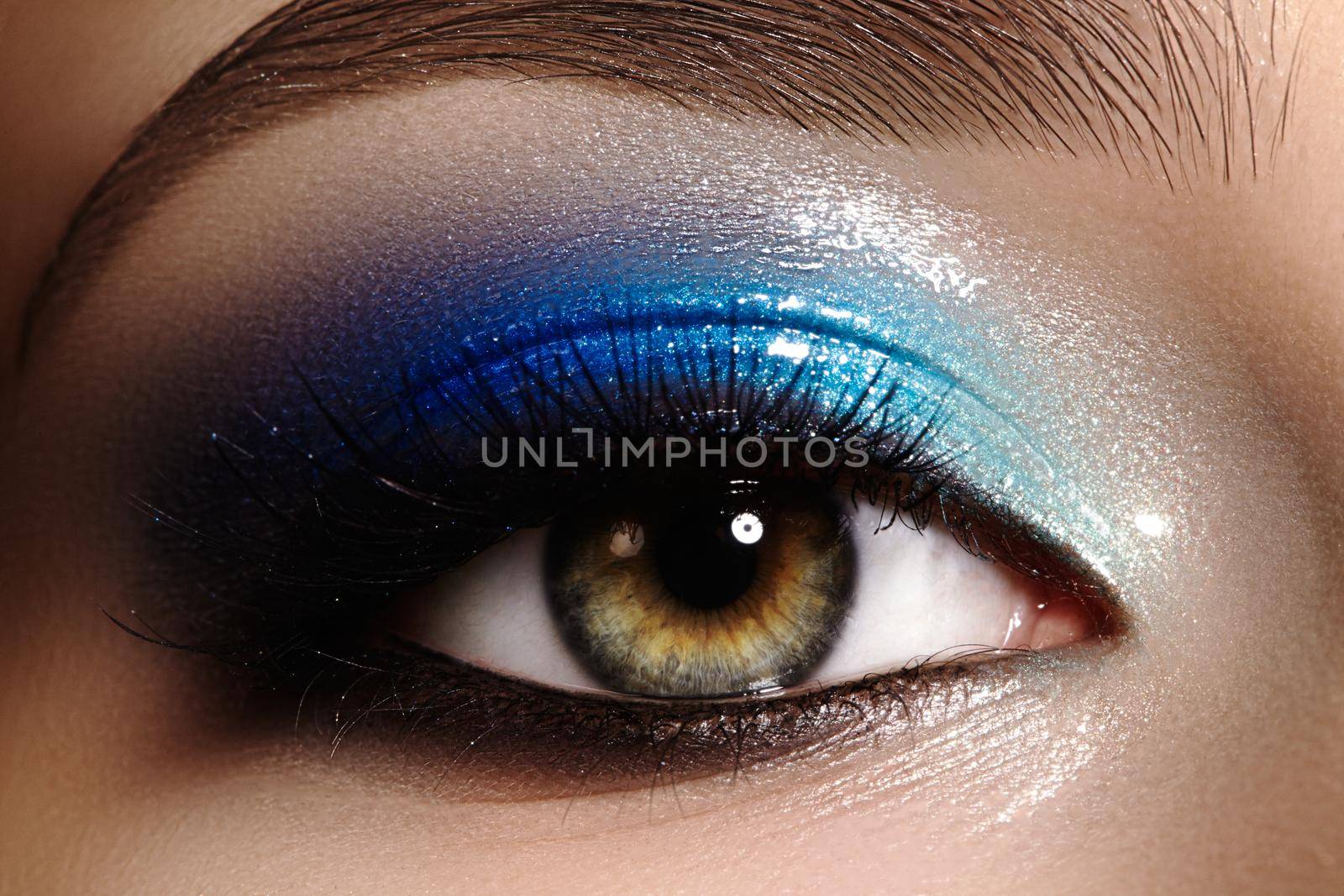 Closeup female eye with beautiful fashion bright make-up. Beautiful shiny blue eyeshadow, wet glitter, black eyeliner, perfect eyebrows shape.