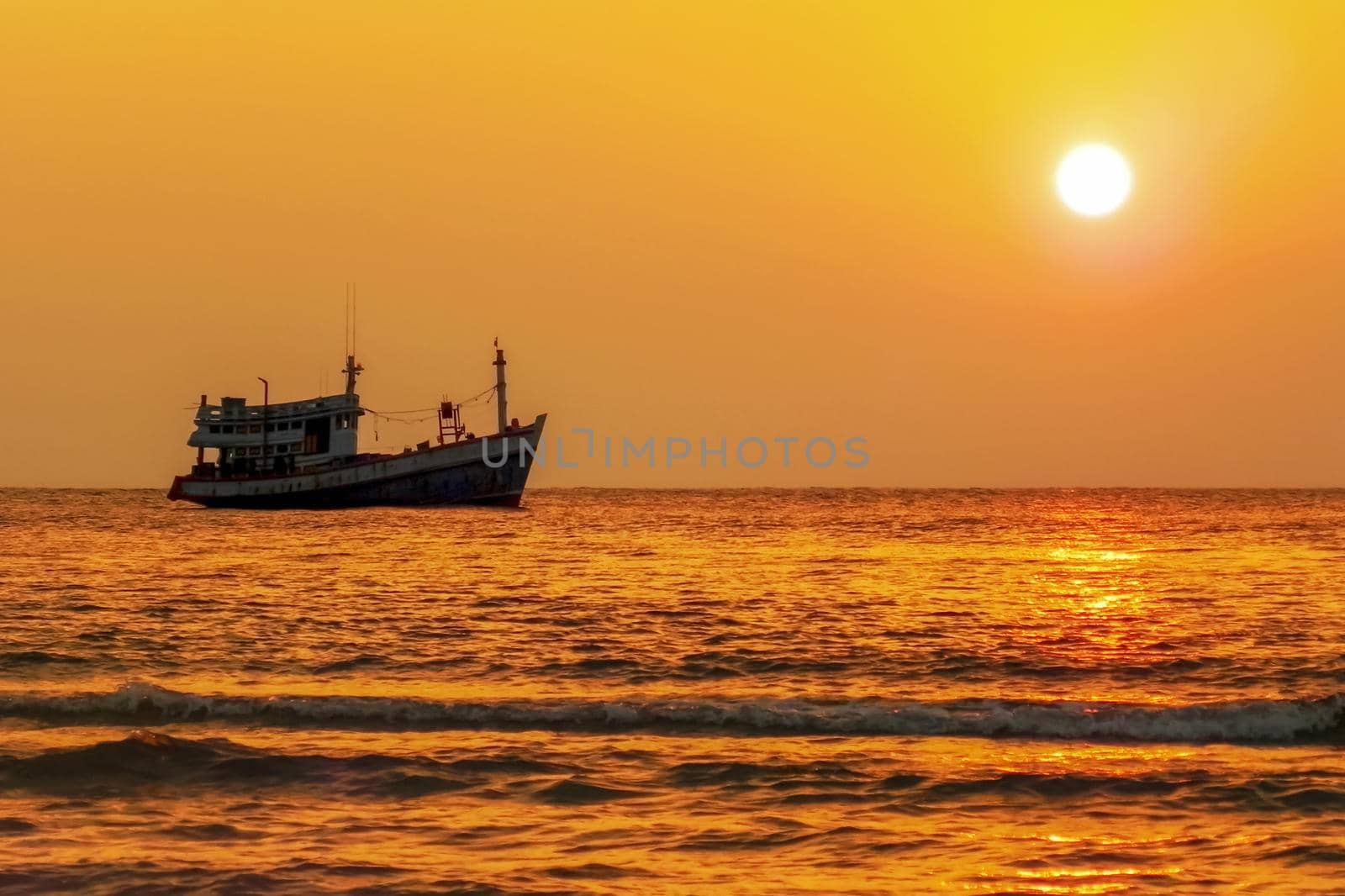 Fishing boat at sea on the horizon during sunset.