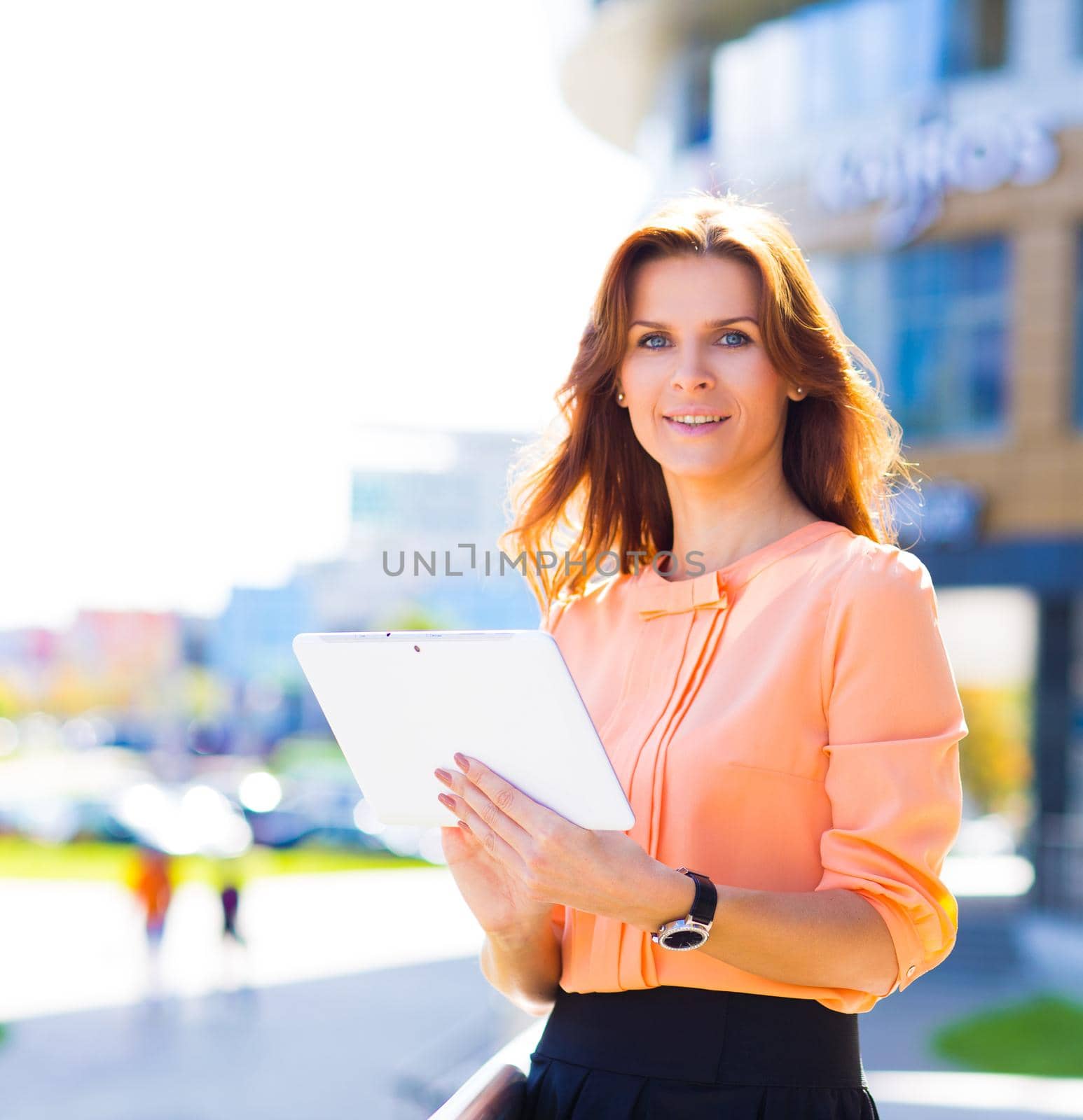 Portrait of pretty businesswoman in smart casual using digital tablet outdoors