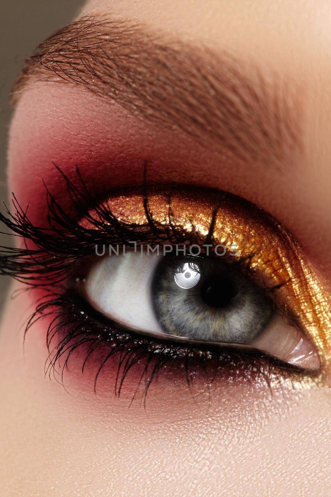 Closeup female eye with fashion bright make-up. Beautiful gold, red eyeshadow, wet glitter, black eyeliner. Perfect Shape of Eyebrows