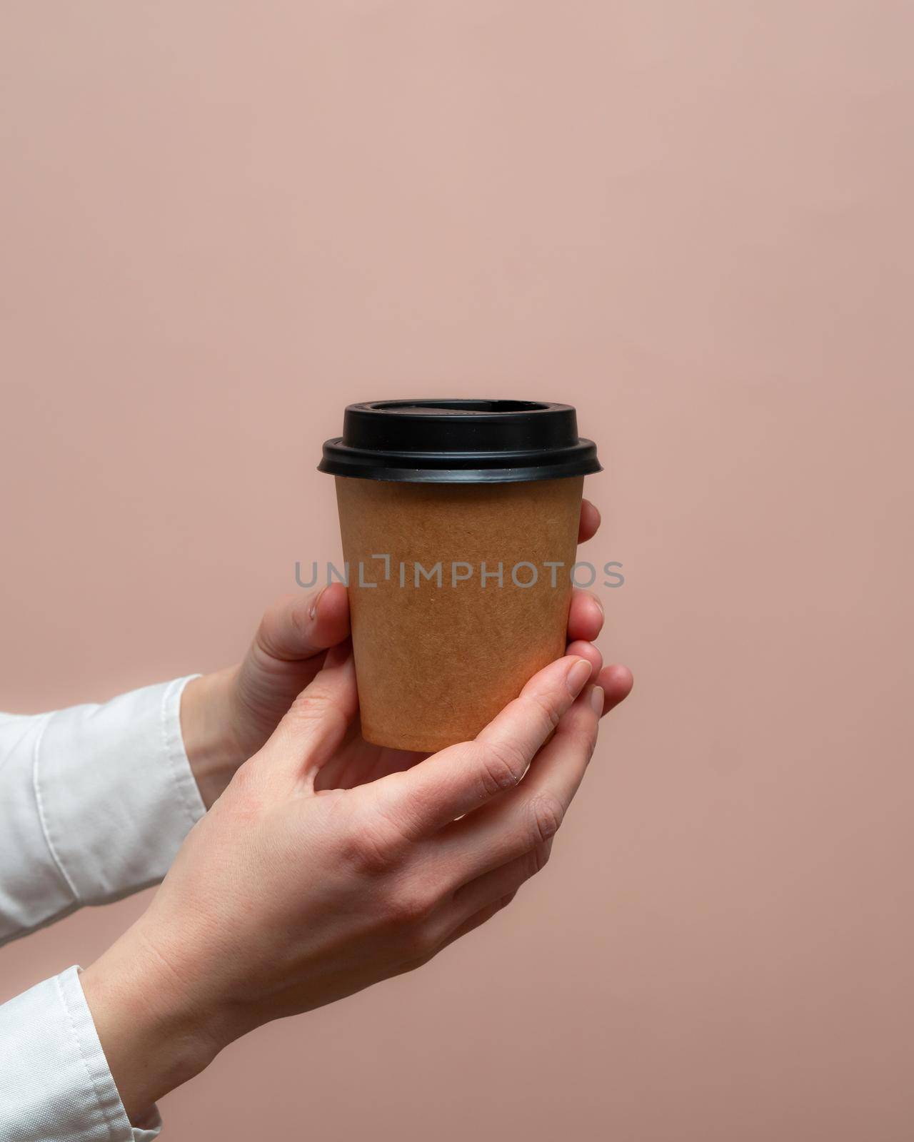 Woman hands hold paper cup on pink background. Copy space.