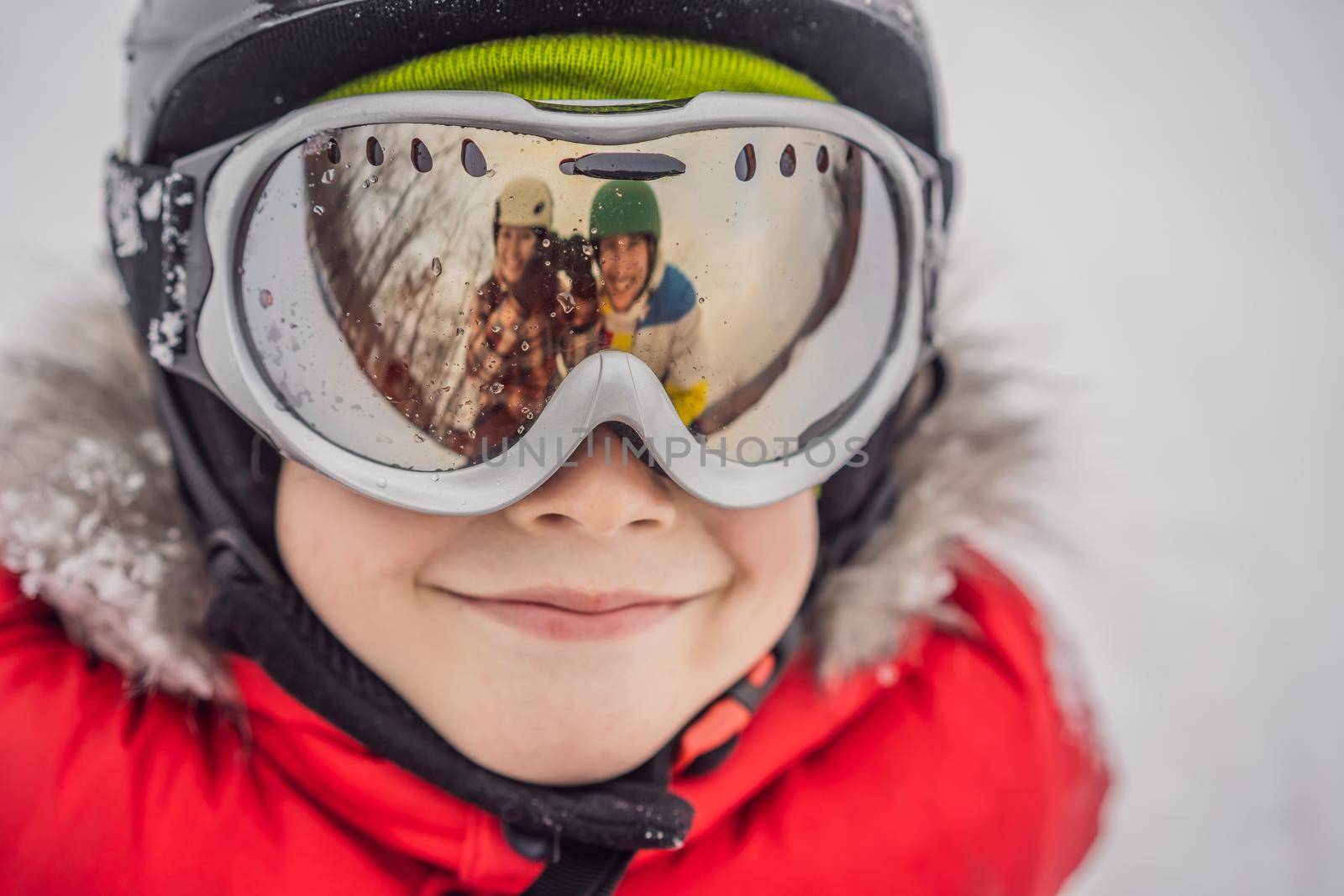 Mom and Dad are reflected in the boy ski goggles. Mom and Dad teach a boy to ski or snowboard.