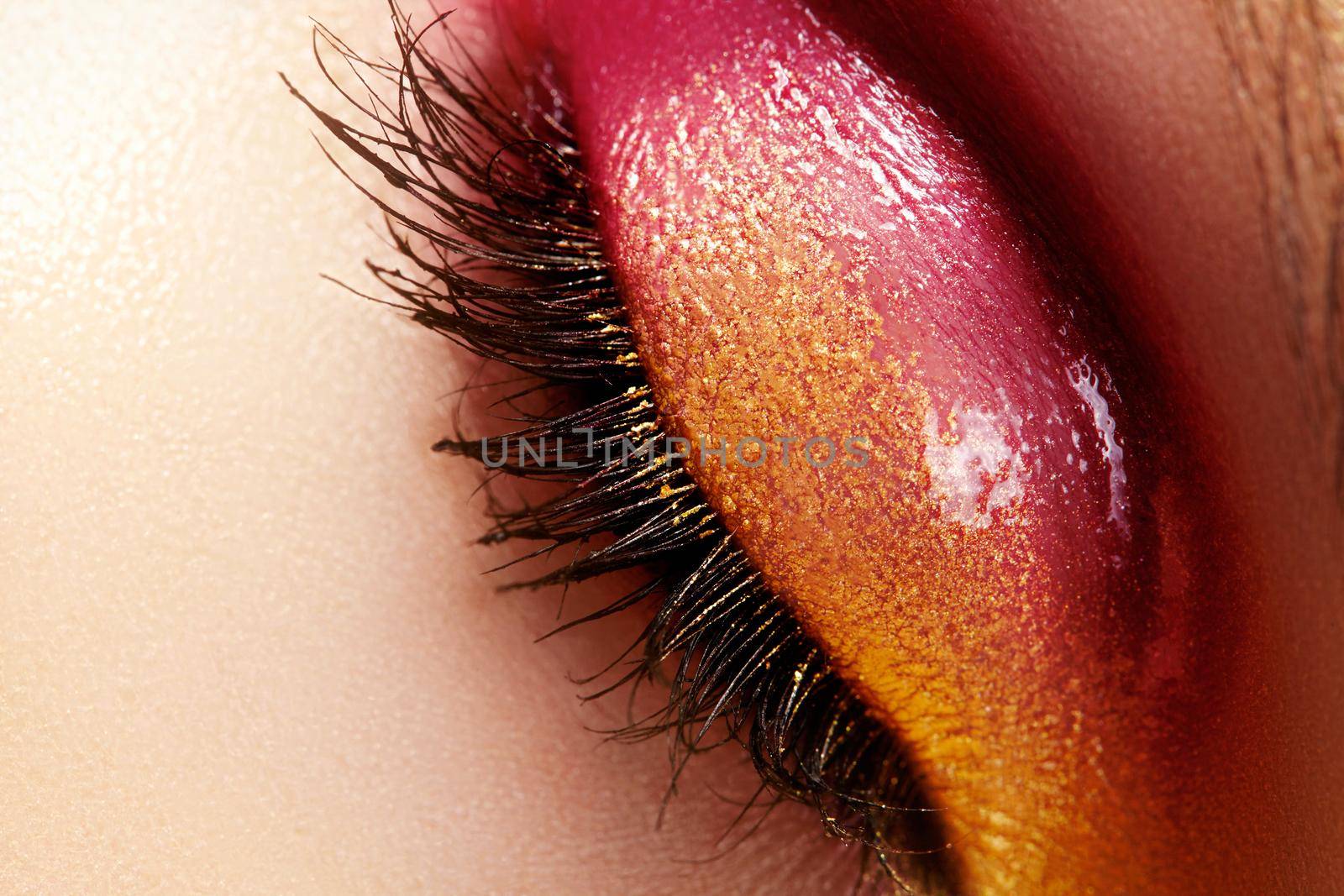 Closeup female eye with beautiful fashion bright make-up. Beautiful shiny gold, pink eyeshadow, wet glitter, black eyeliner