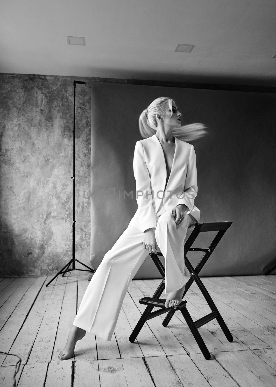 High Fashion blond woman in white suit. Elegant Style model. Dynamic shot in Photo studio shooting. Black and white