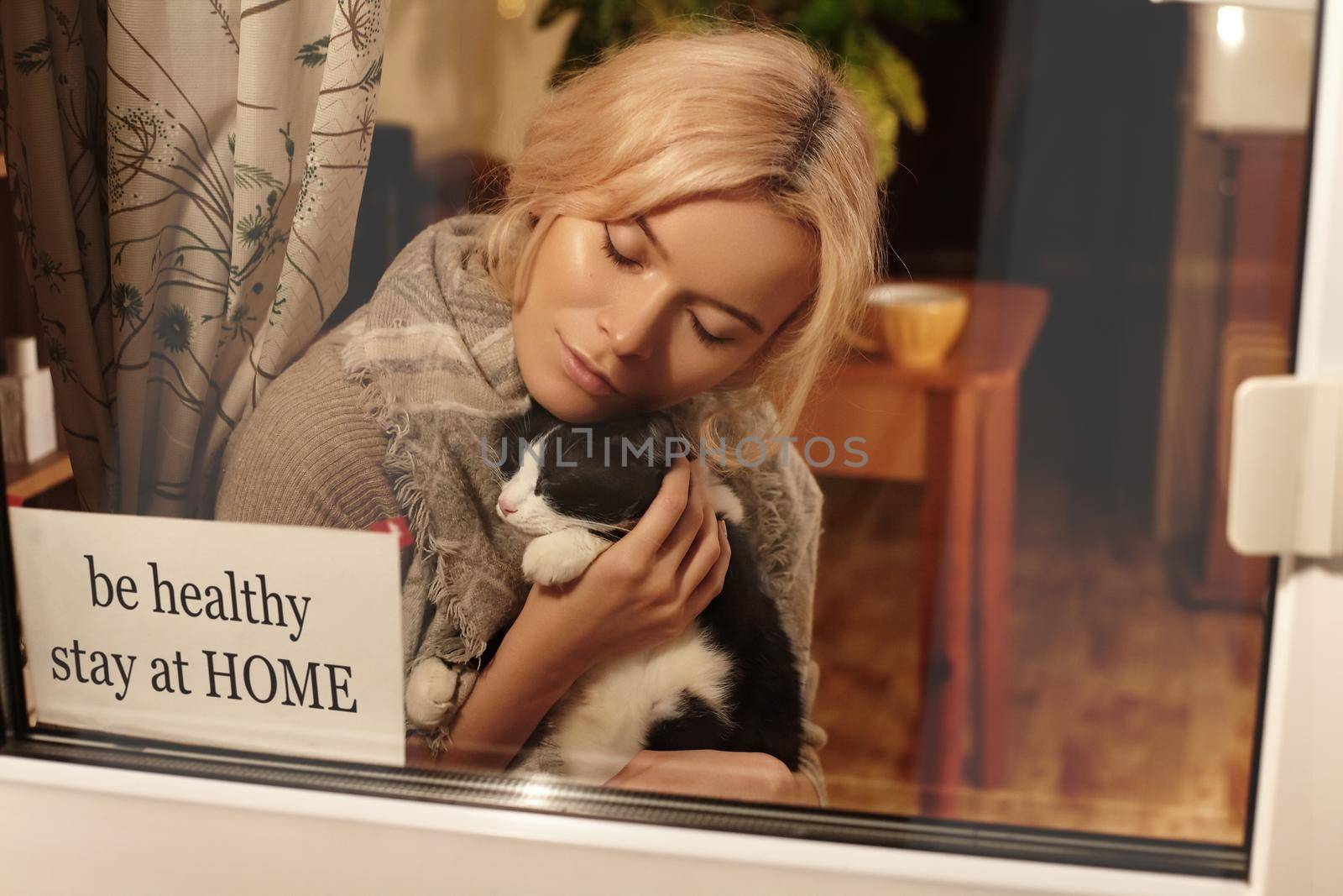 Be Healthy, Stay Home. Woman blonde in home clothing in apartment with cute cat in her arms stay at home. Self isolating while quarantine concept. Stop virus