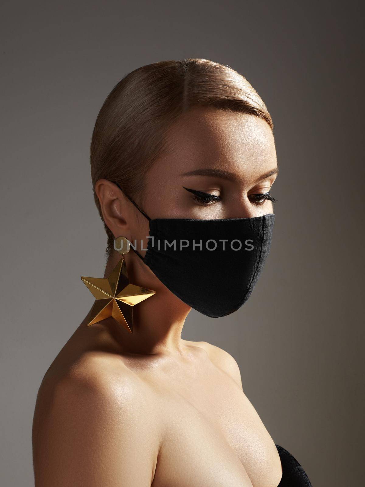 Beautiful woman with a black medicine mask on face. Fashion eye make-up, celebrate style, gold jewelry. Beauty with protection hygiene in viral covid-19 pandemic. Party christmas stylish