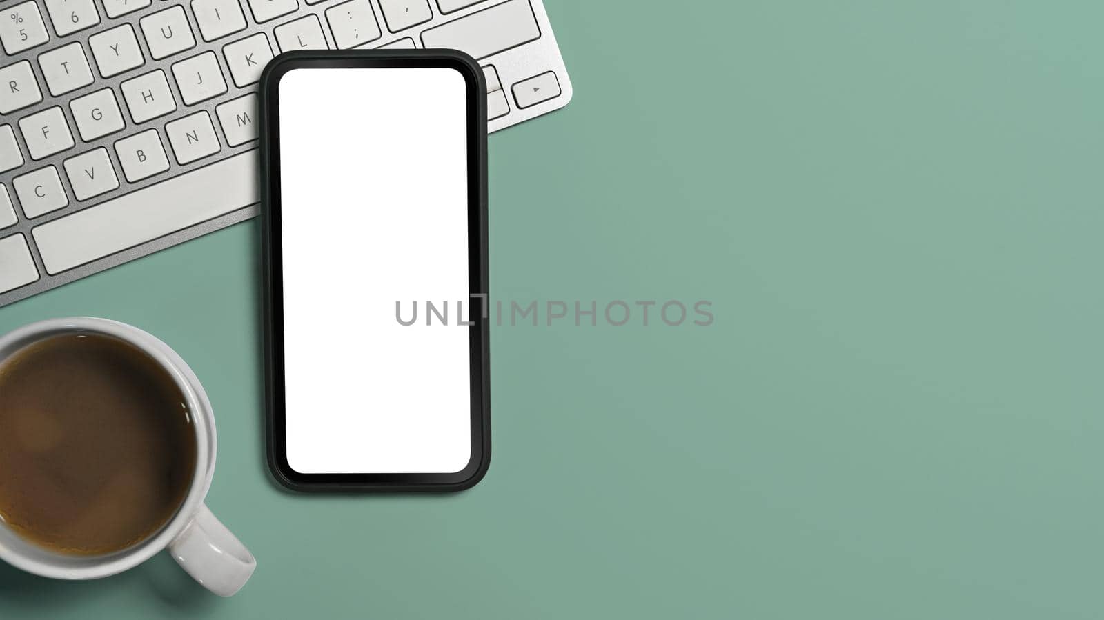 Flat lay smart phone, coffee cup and keyoard on green background. Copy space, blank screen for advertise text by prathanchorruangsak