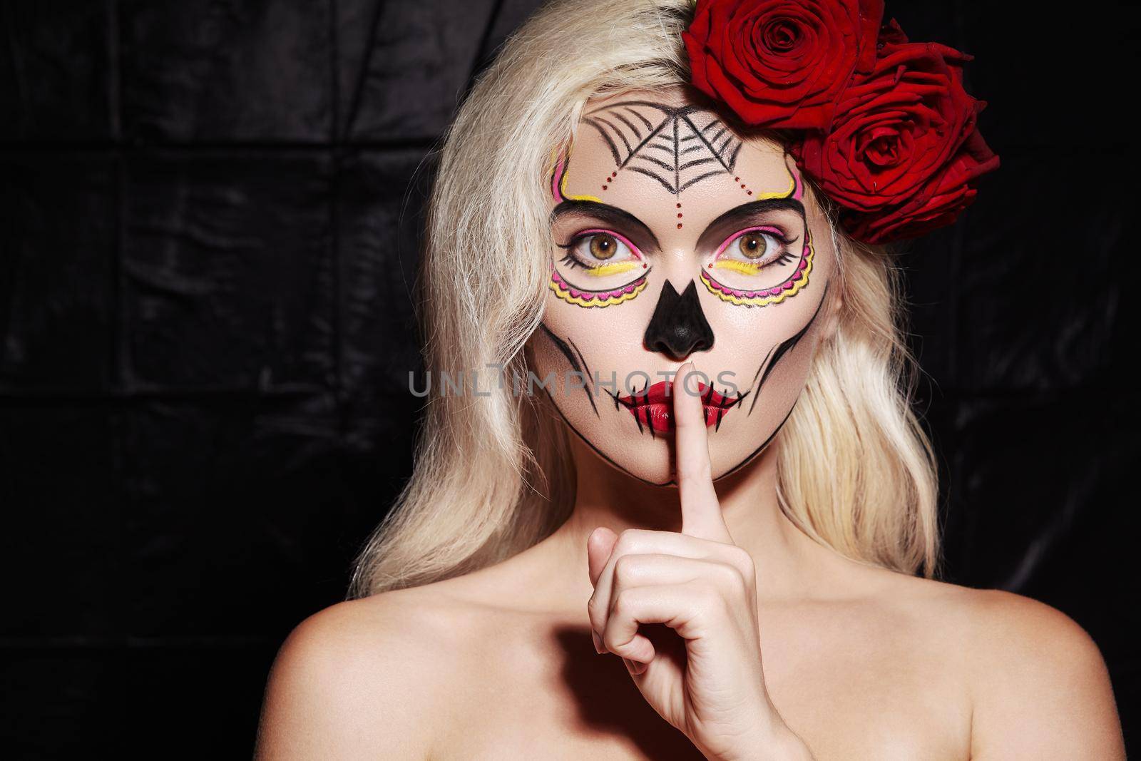 Halloween Make-Up Style. Blond Model Wear Sugar Skull Makeup with Red Roses. Santa Muerte Concept. Silence Gesture by MarinaFrost