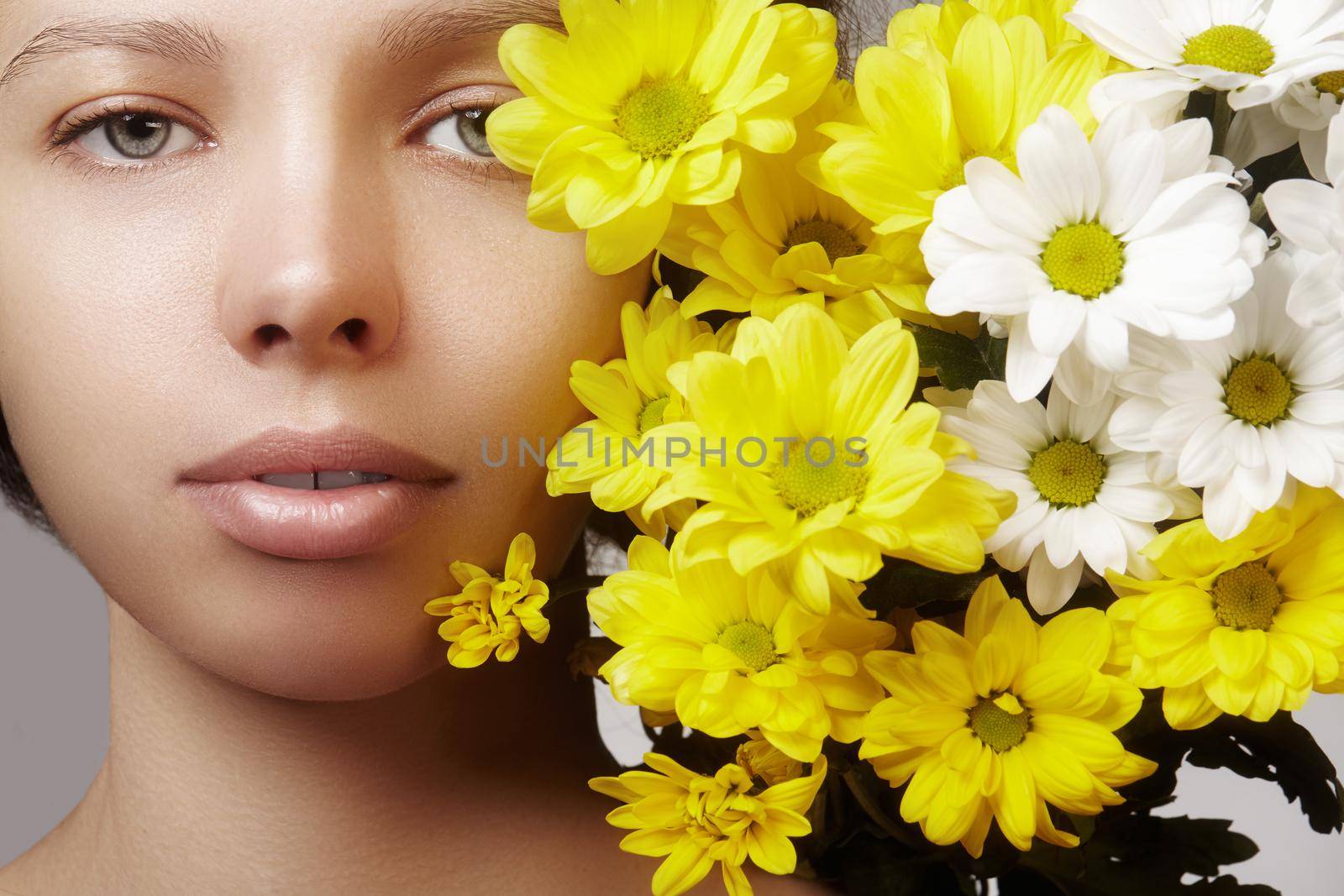 Beautiful young woman with perfect clean shiny skin, natural fashion makeup with spring flowers. Close-up woman, fresh spa look.