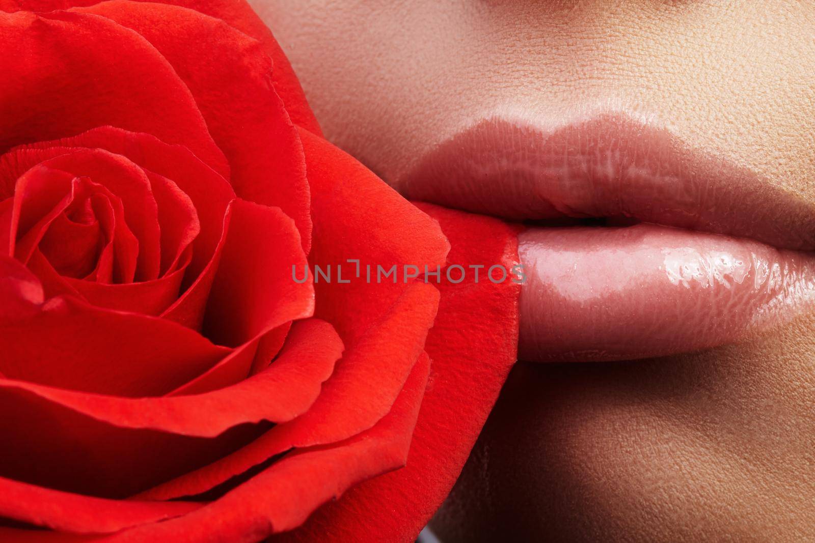 Close-up beautiful female lips with bright lipgloss makeup. Perfect clean skin, light fresh lip make-up. Beautiful spa portrait with red rose flower. Spa and cosmetics