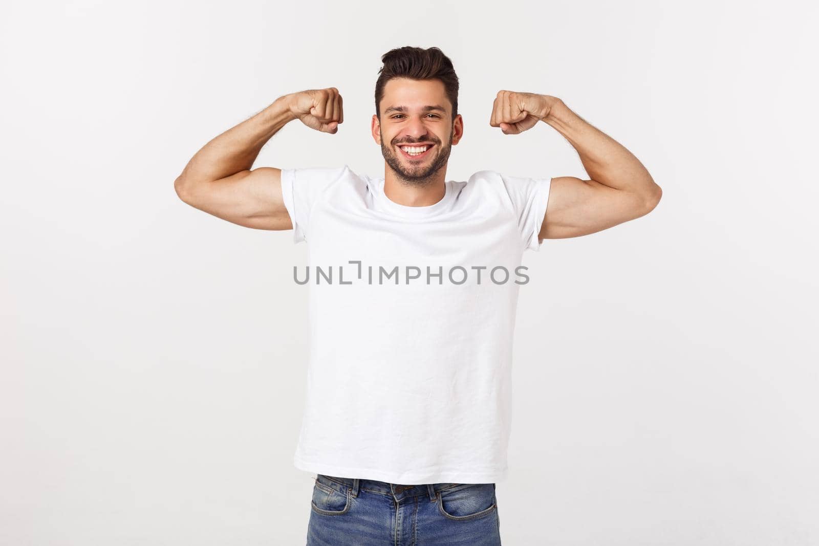 Handsome fit young funny bearded man pointing to his bicep and smiling on white background.