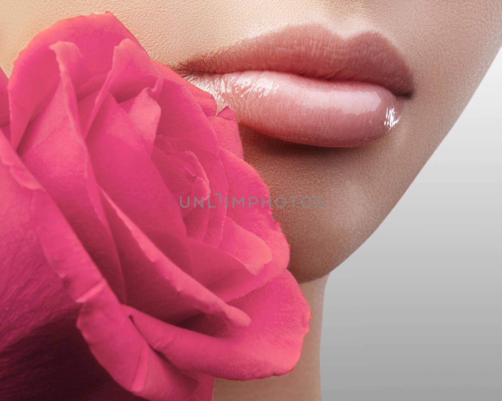 Close-up beautiful female lips with bright lipgloss makeup. Perfect clean skin, sexy red lip make-up. Beautiful visage portrait with red rose flower. Visage and cosmetics