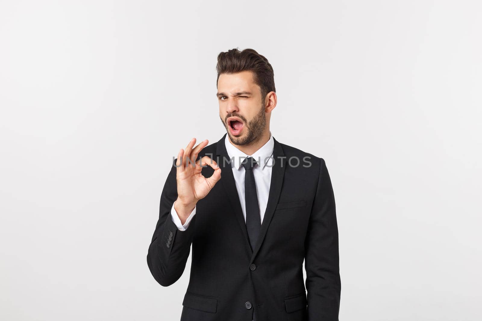 Handsome smiling businessman showing ok sign with fingers over gray background