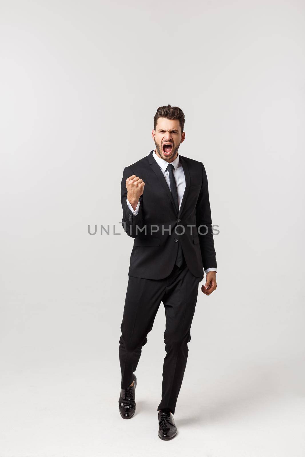 Cheerful young bearded business man show hand up excited with clenched fists. Full length portrait business man isolated over white studio background.