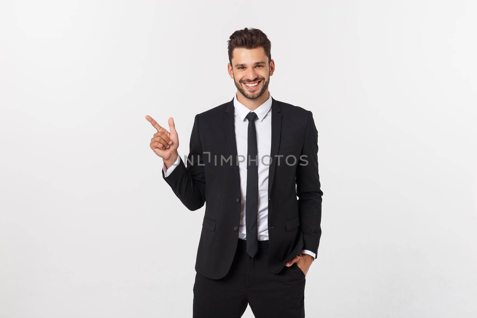 Portrait of young business man in suit pointing at copy space over white background. by Benzoix