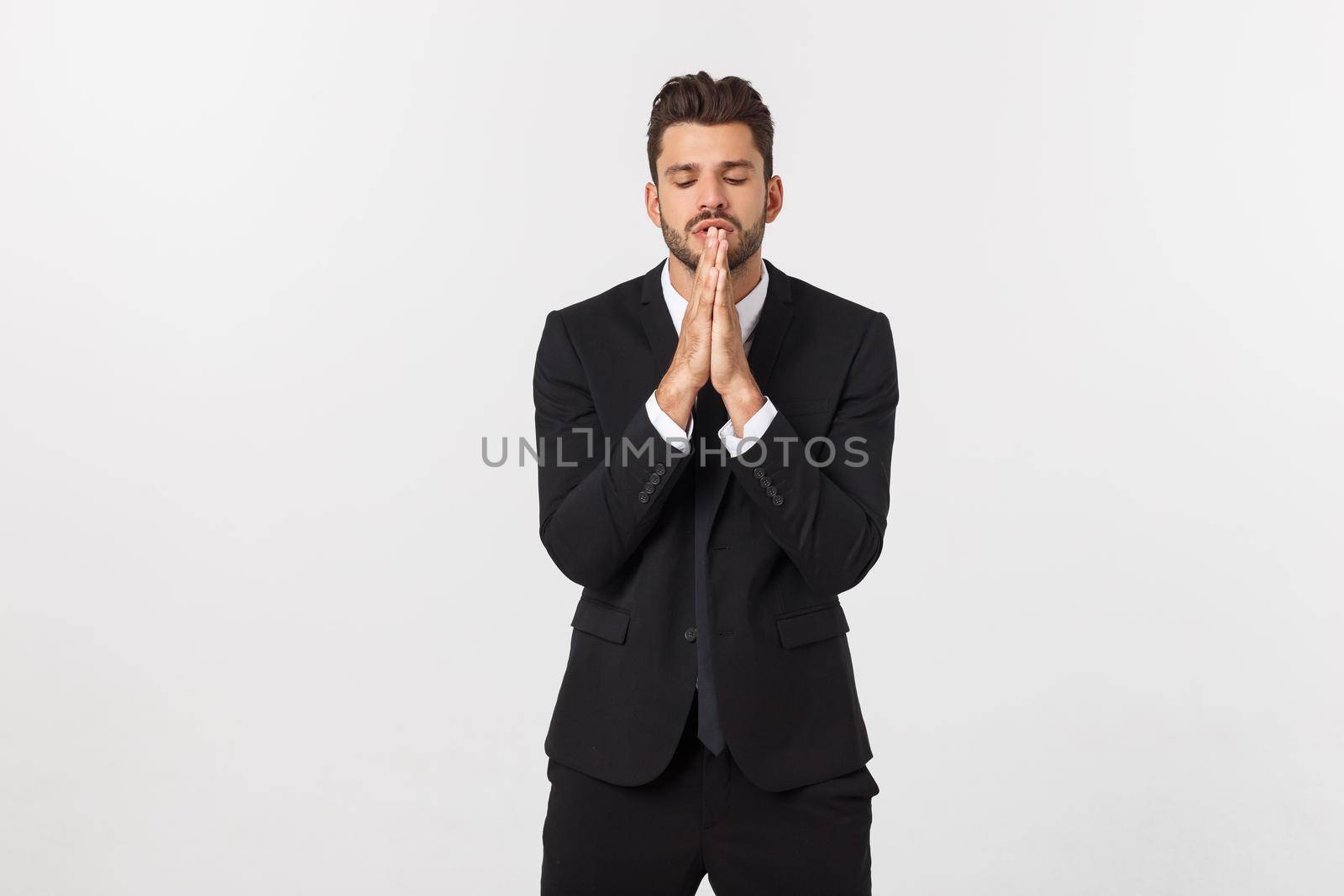 Handsome young business man standing praying, isolated over white background. Concept of idea, ask question, think up, choose, decide