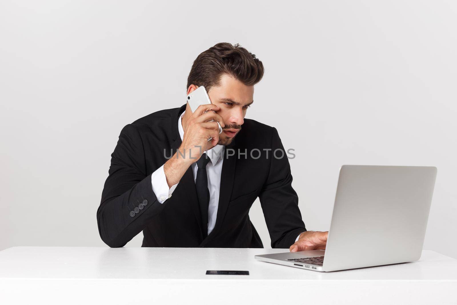 Caucasian attractive businessman worried and tired talking on mobile phone sitting at office desk working in stress overworked and frustrated. by Benzoix