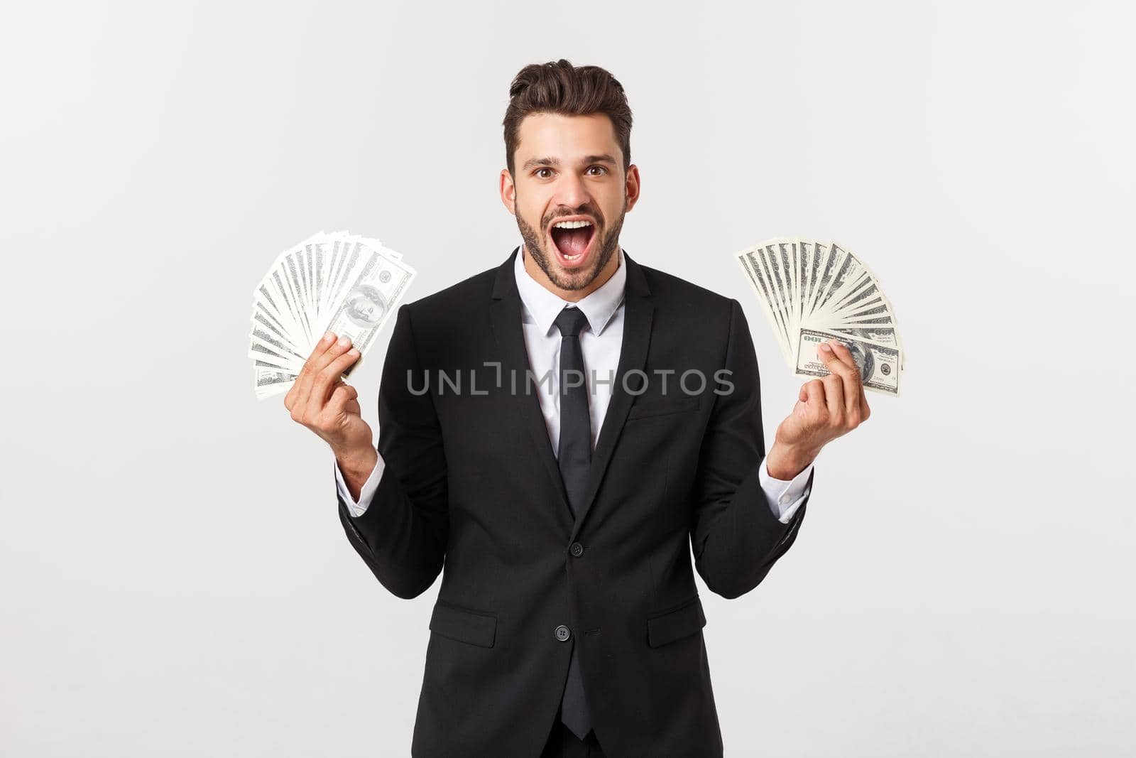 Portrait of a satisfied young businessman holding bunch of money banknotes isolated over white background. by Benzoix