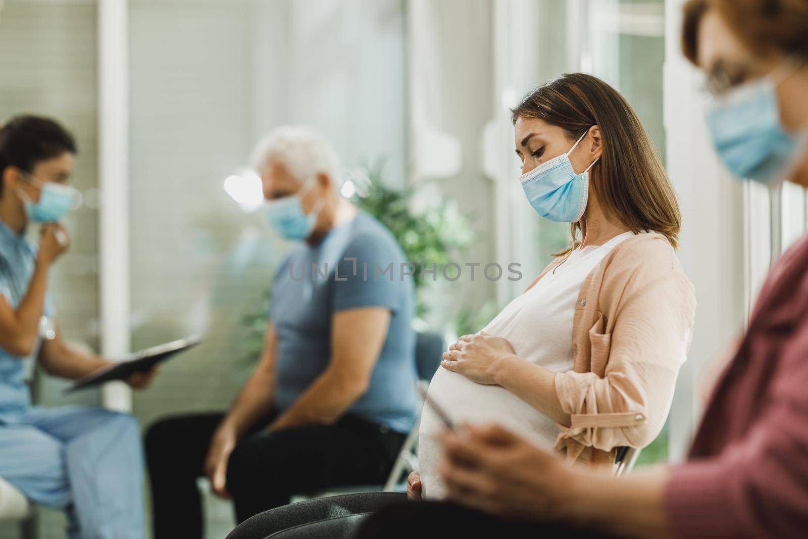Young pregnant woman with a face mask sitting in a waiting room and waiting medical exam during corona virus pandemic.