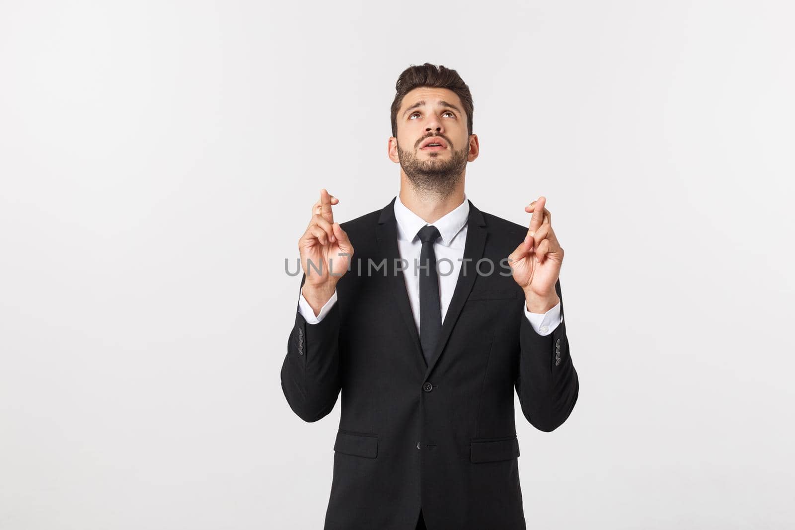 Businessman fingers cross on copy space. Handsome young man in suit looking at camera while standing against white background