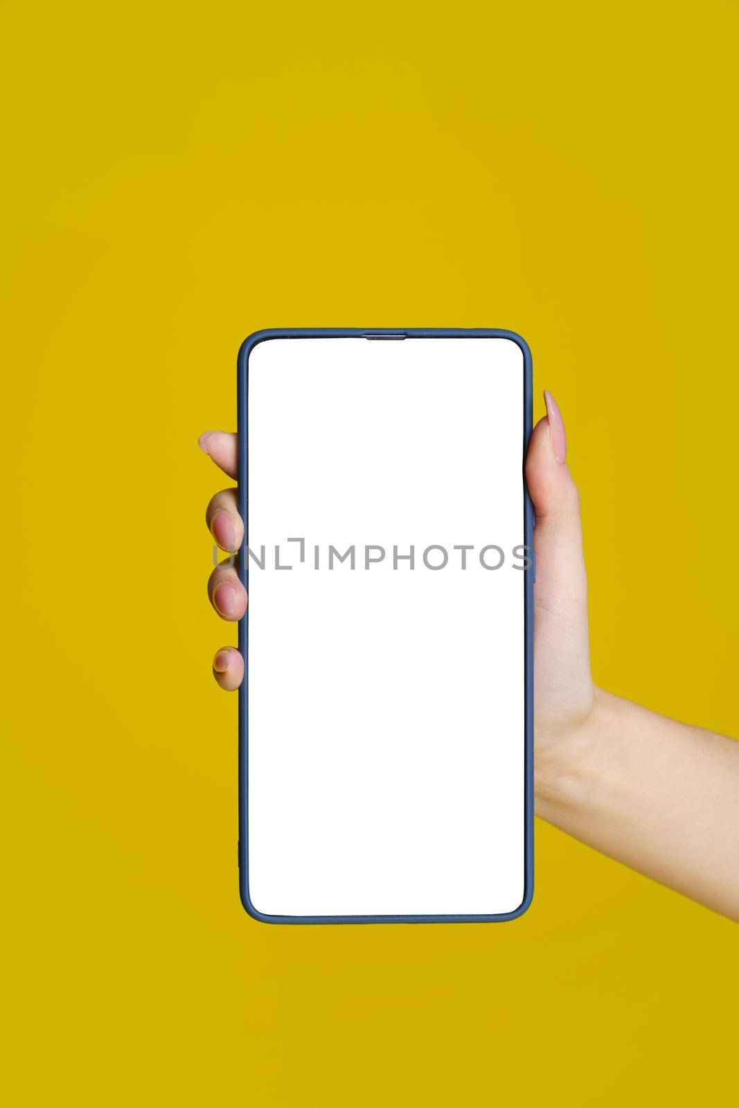 Close up woman hand holding smartphone with green screen and blue phone case. Isolated on yellow background. Mobile phone frameless design concept. Mobile app advertising. Copy space. Great offer by LipikStockMedia