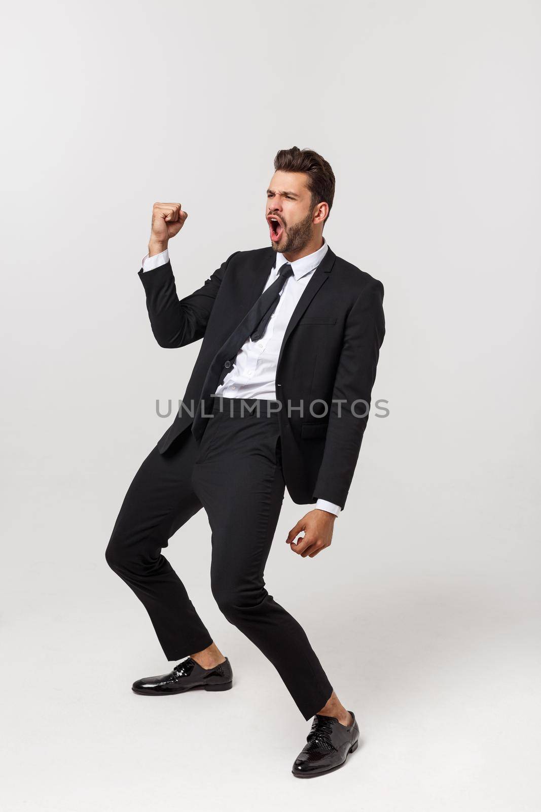 Cheerful young bearded business man show hand up excited with clenched fists. Full length portrait business man isolated over white studio background by Benzoix