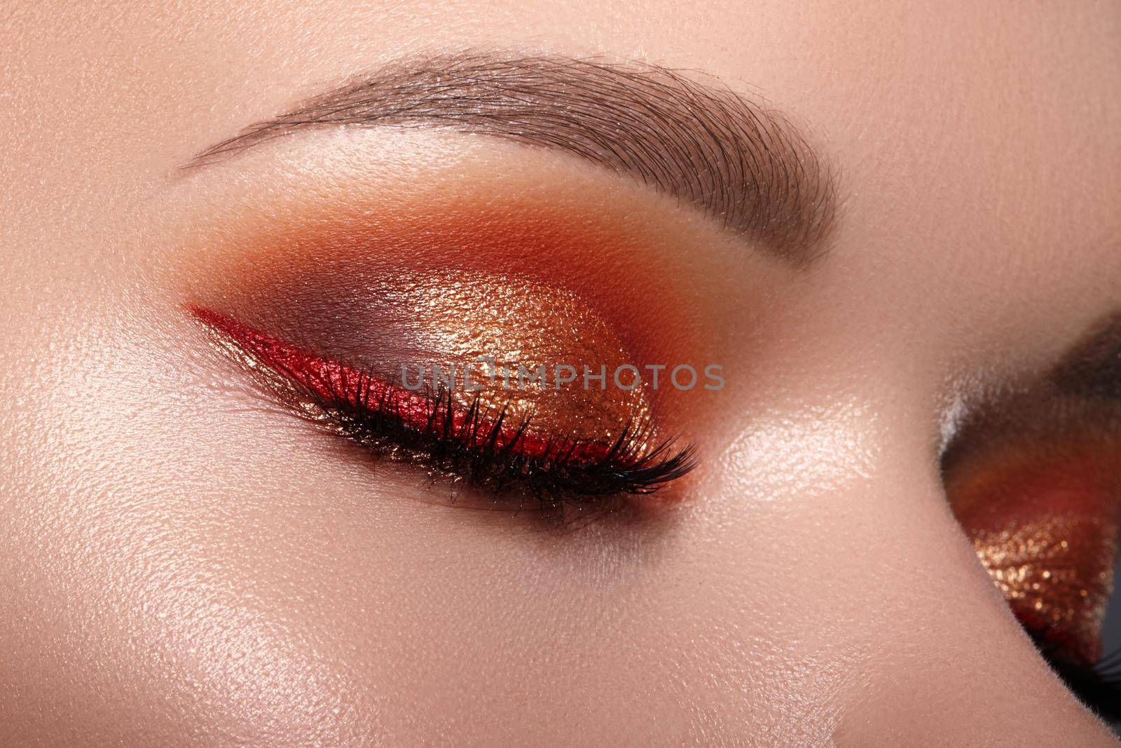 Closeup of Woman Face with Eyes Make-up. Fashion Celebrate Makeup with Red Liner, Gold Shadows, Glowy Clean Skin, perfect Shapes of Brows. Macro of Female Eye. Halloween Style