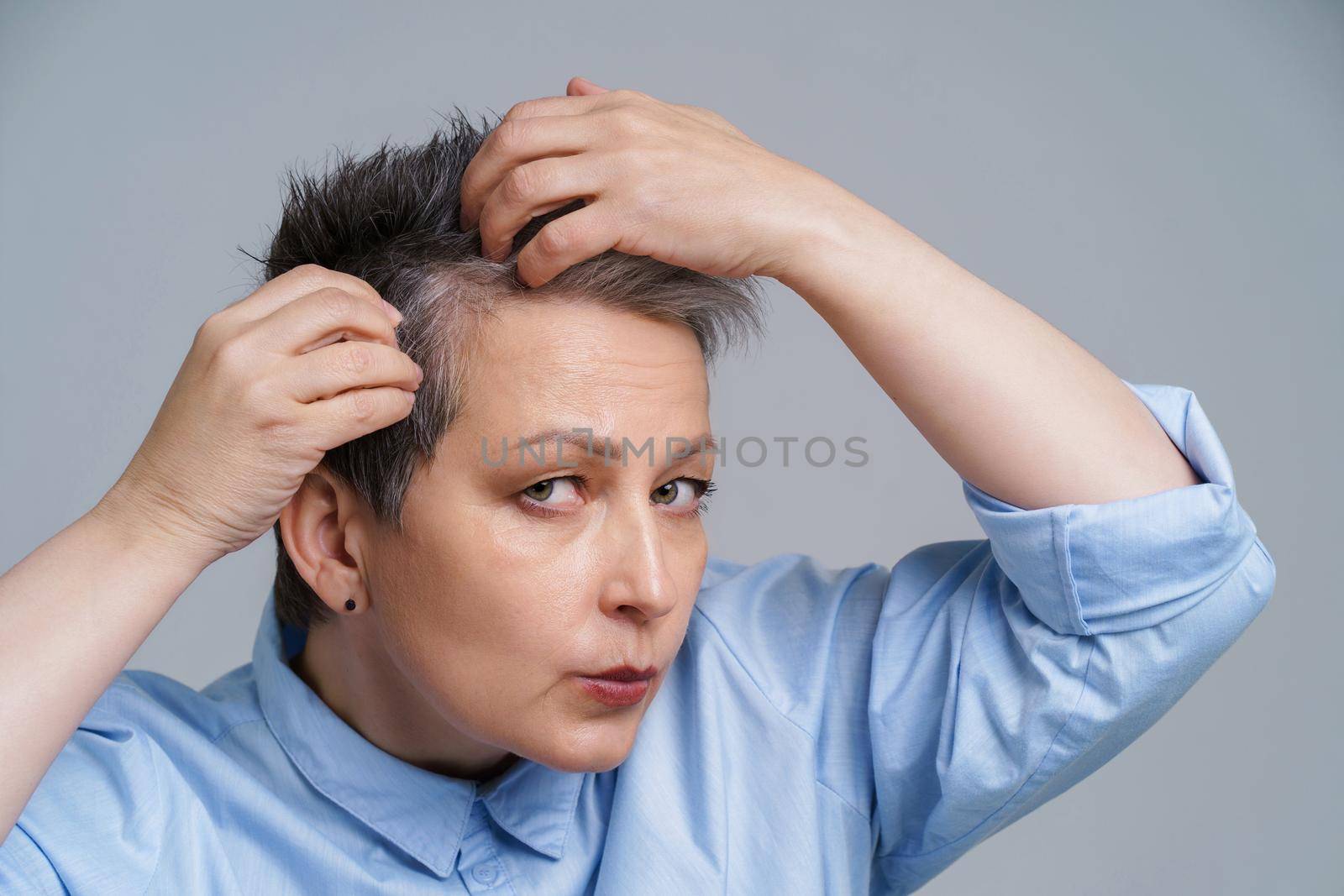 Portrait of mature woman in 50s checking her hair and unhappy to see a results in mirror. Beautiful grey haired woman dealing with dandruff problem checking in mirror.