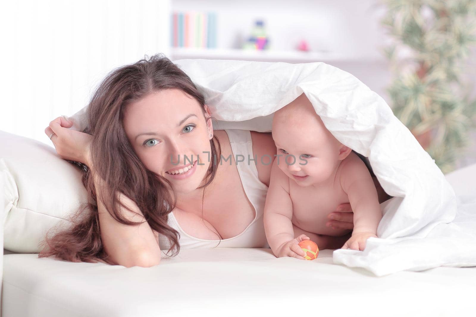 mom plays with the baby lying on the bed by SmartPhotoLab