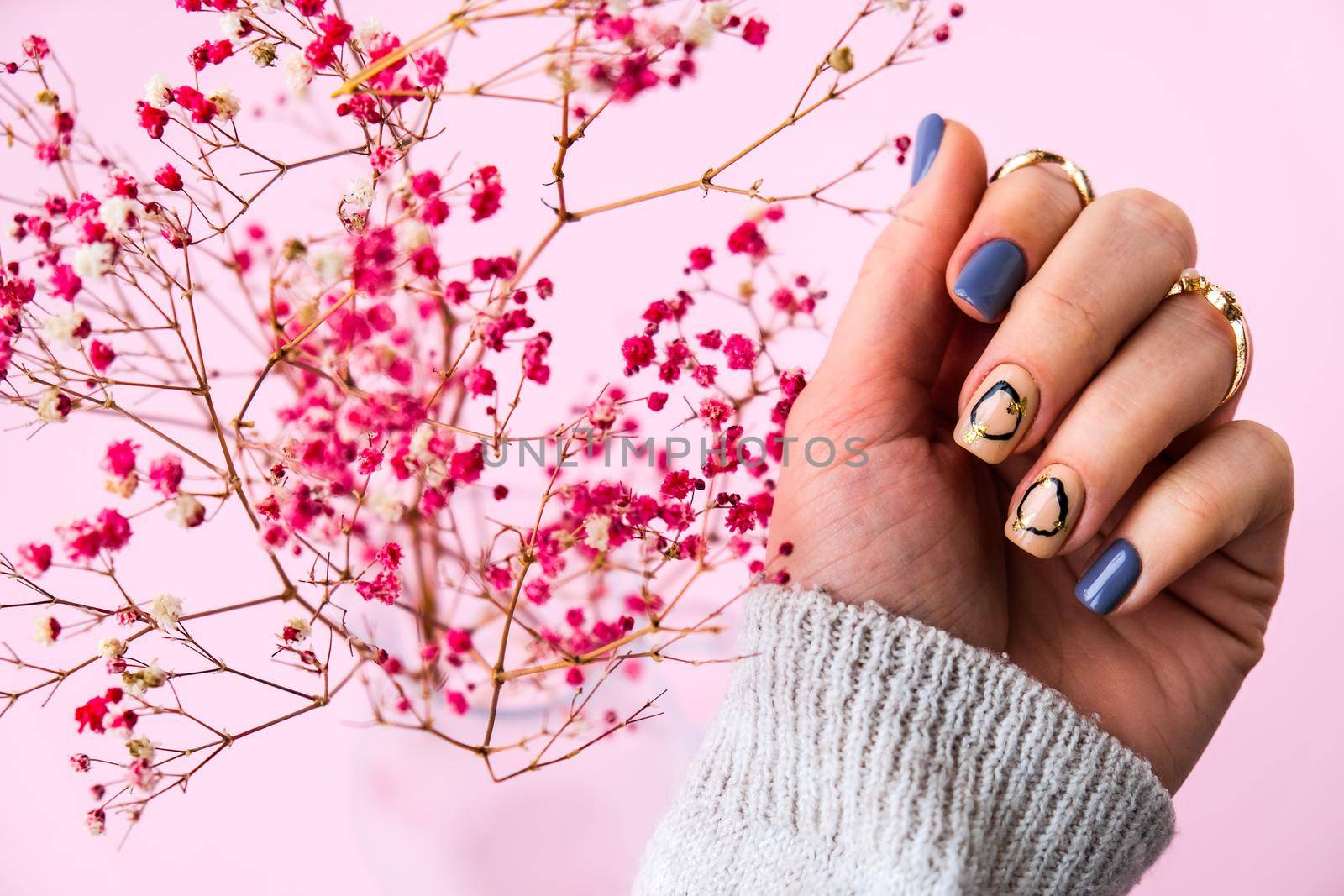 Hand in sweater and pink flowers with modern manicure nails. Female hand. Glamorous beautiful manicure. Manicure salon concept. Nail polish close up.