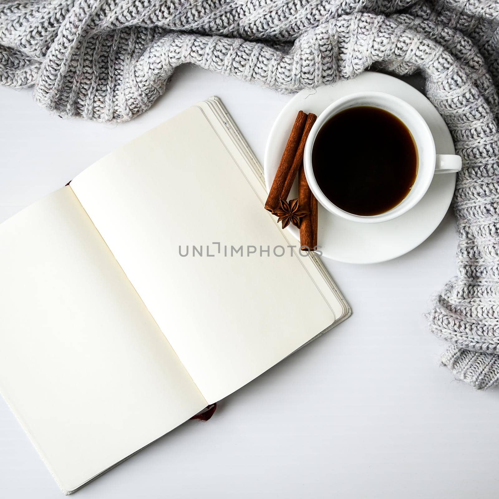 Cup of coffee with notebook cinnamon sticks and anise star on white background. Sweater around. Winter morning routine. Coffee break. Copy space. Top view. Breakfast. Flat lay