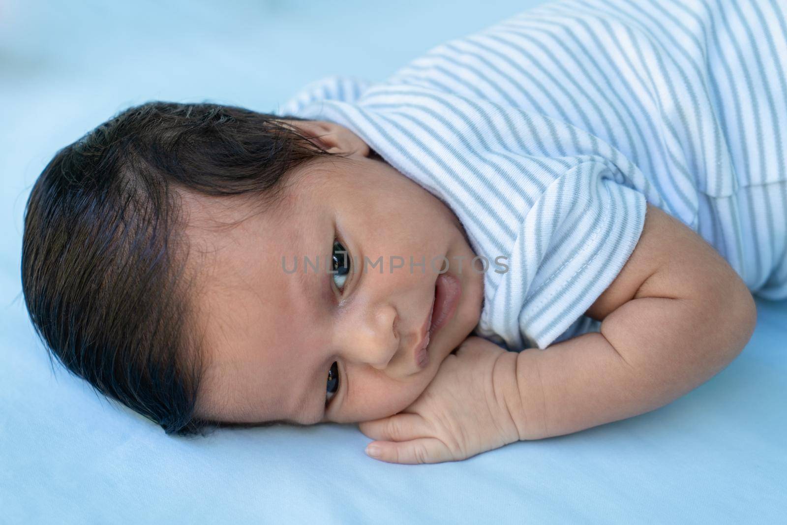 Infant lying on his stomach with his eyes open on a blue diaper