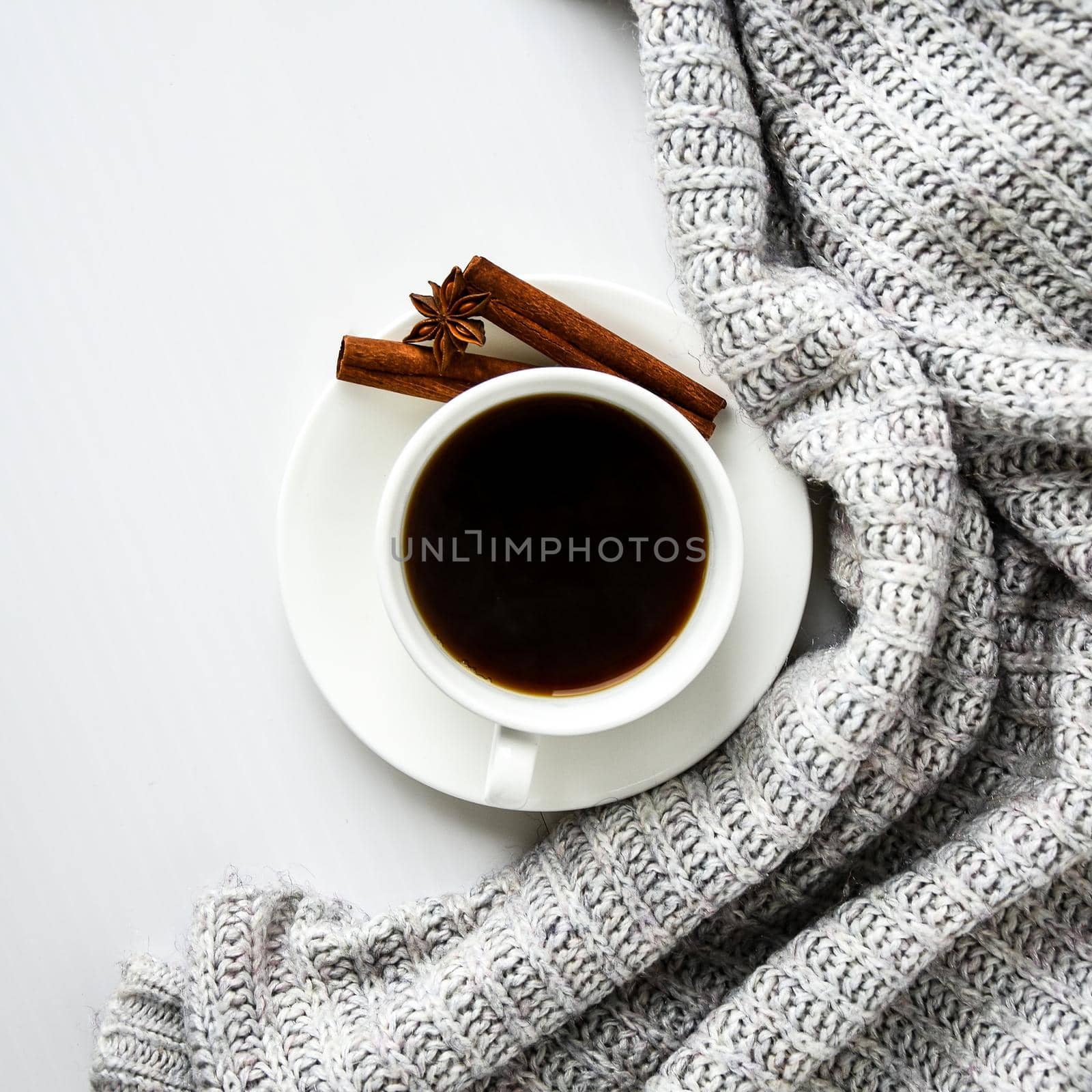 Cup of coffee with cinnamon sticks and anise star on white background. Sweater around. Winter morning routine. Coffee break. Copy space. Top view. Flat lay by anna_stasiia