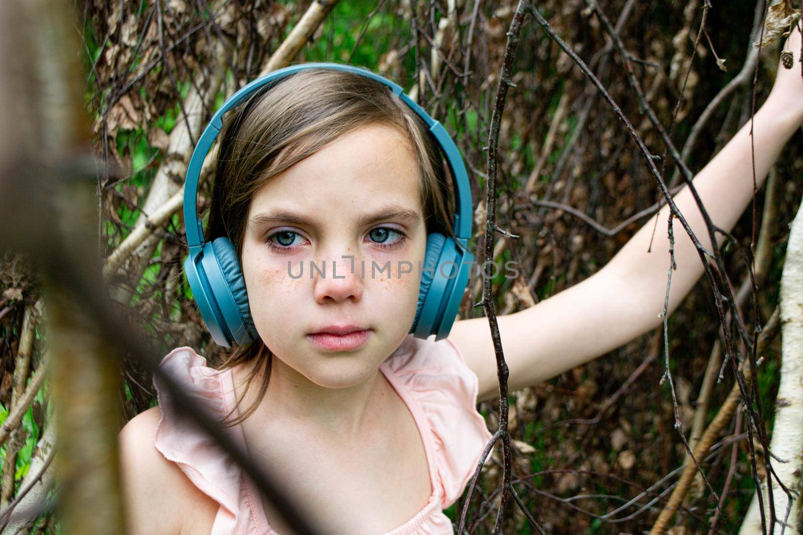 Young beautiful girl fooling around with a branch and wearing headphones on them to listen to music or block out sound due to auditory sensitivity. High quality photo