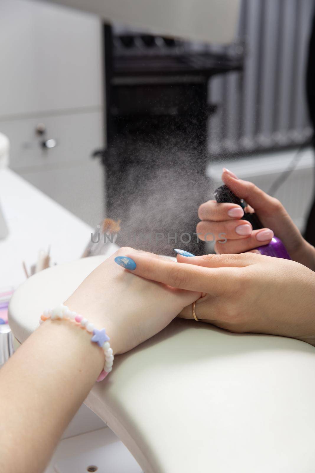 Manicurist sprays antiseptic on the nails before treating old acrylic nails. by BY-_-BY