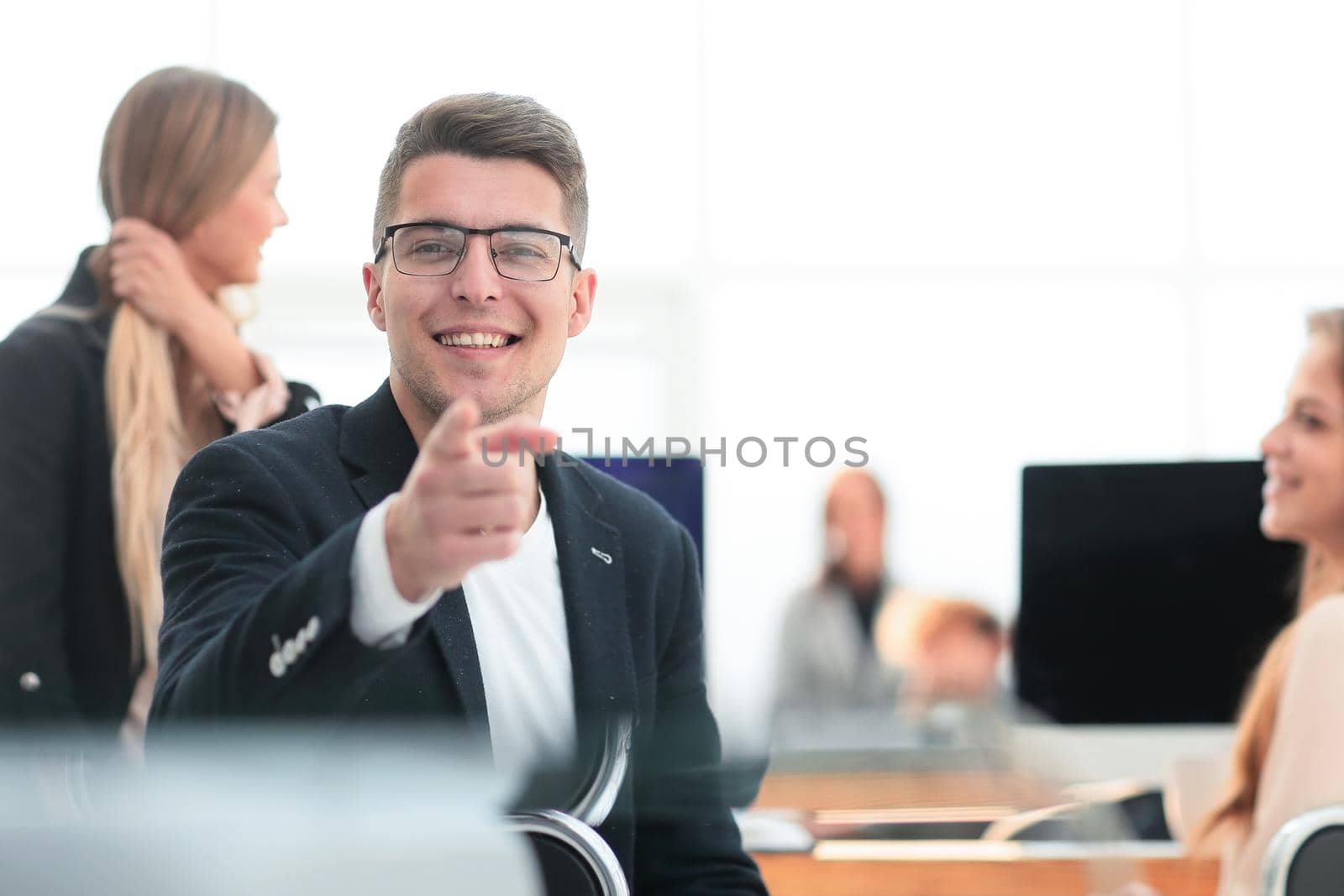 close up. smiling business man sitting at an office Desk and pointing at you.