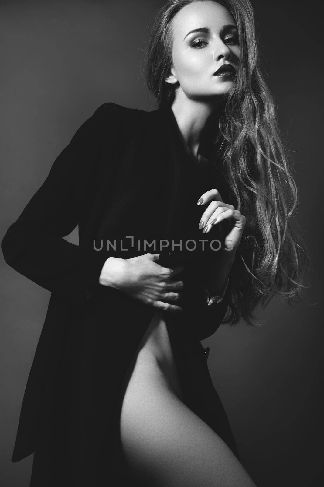 Sexy lady in Elegant Coat. Beautiful model in Fashion Jacket with Long Curly Hair. Erotic style. Black and White shot on grey background