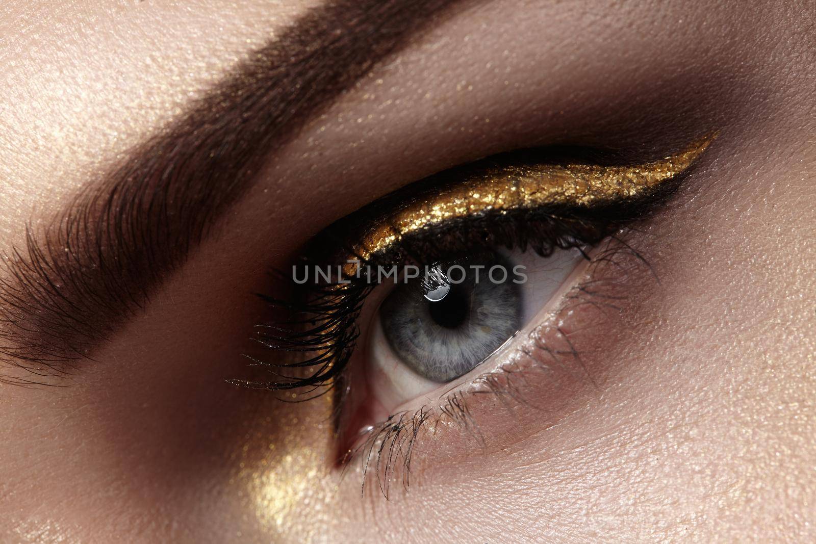 Beautiful macro shot of female eye with ceremonial makeup. Perfect shape of eyebrows, eyeliner and pretty gold line on eyelid. Cosmetics and make-up. Closeup macro shot of fashion sparcle visage
