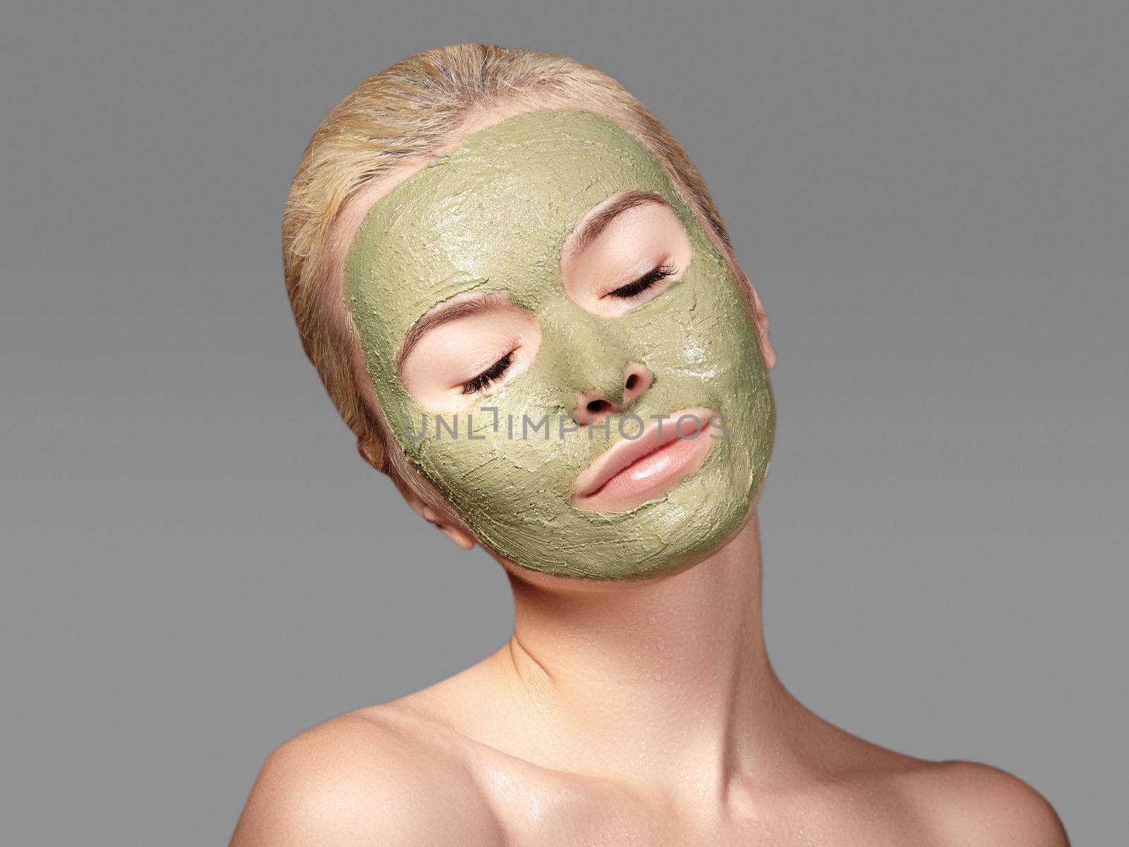 Beautiful Woman Applying Green Facial Mask. Beauty Treatments. Close-up Portrait of Spa Girl Apply Clay Facial mask on grey background