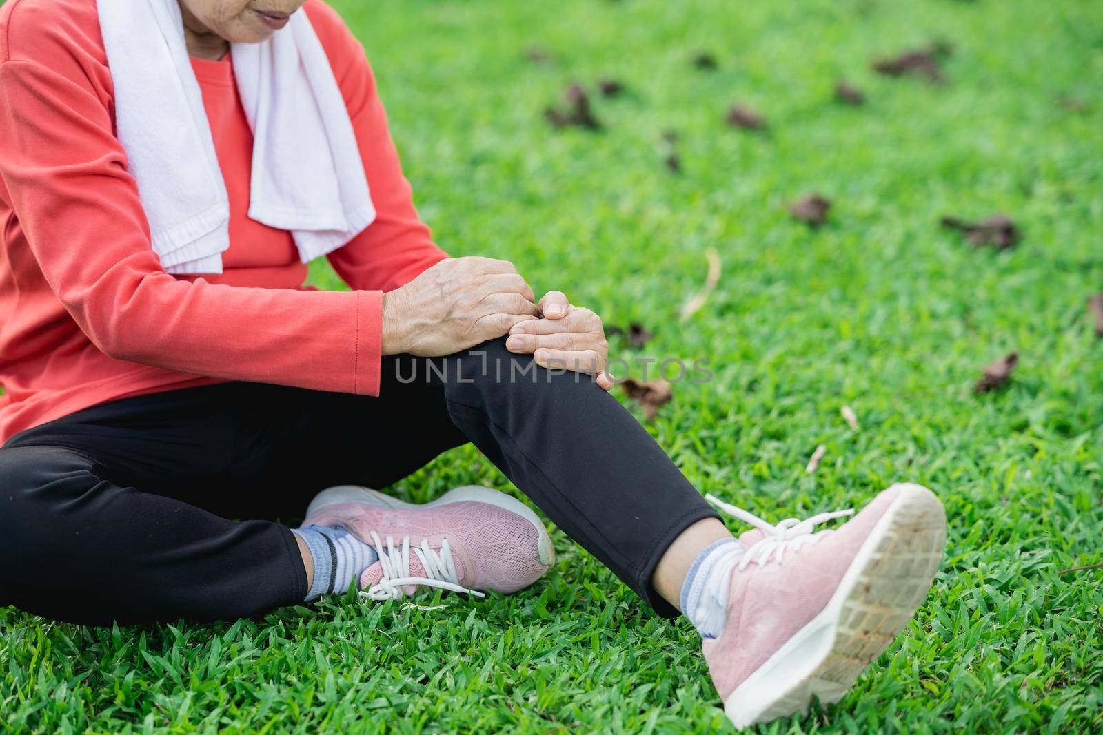 Senior asian woman with knee ankle pain while running in park. Senior asian woman sitting on the ground and holding painful knee. by Wmpix