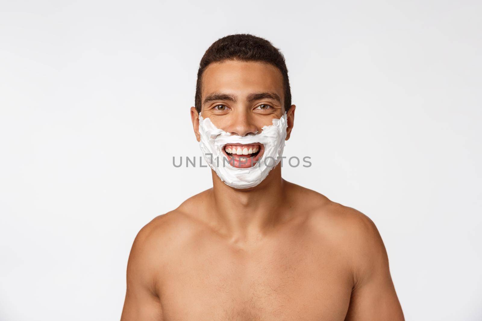 Close up of a happy naked african man with face in shaving foam isolated over gray background.