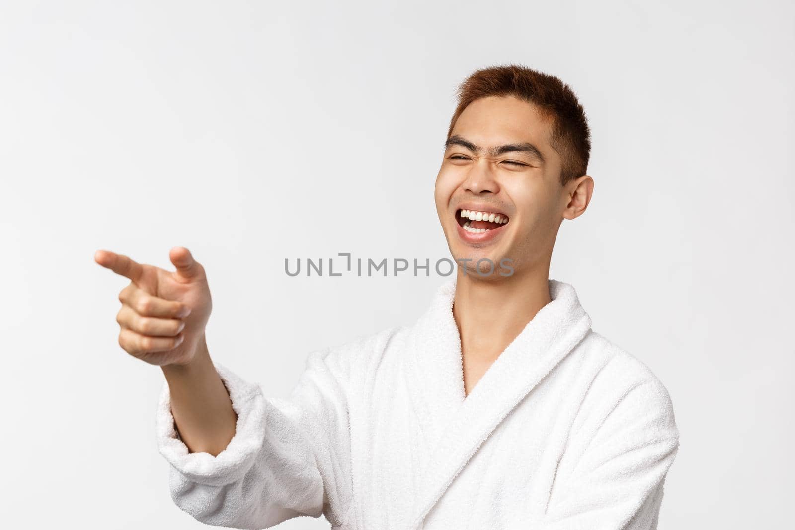 Beauty, spa and leisure concept. Amused, enthusiastic handsome asian man social-distancing, pointing finger left and laughing at something hilarious, watching tv series on quarantine by Benzoix