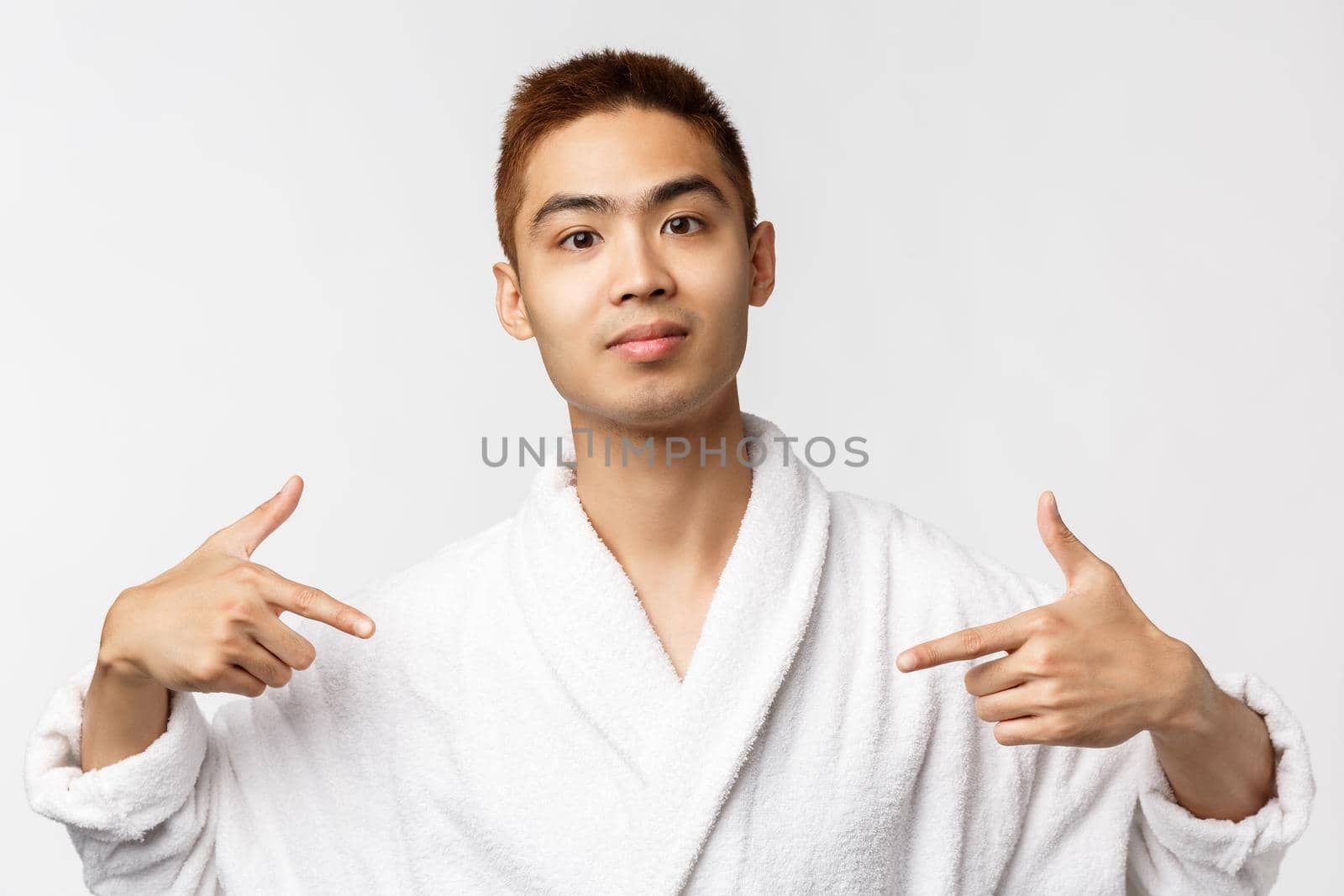 Beauty, spa and leisure concept. Portrait of confident, upbeat smiling asian man in bathrobe, pointing fingers at himself like pro, bragging, being boastful about own achievement, white background.