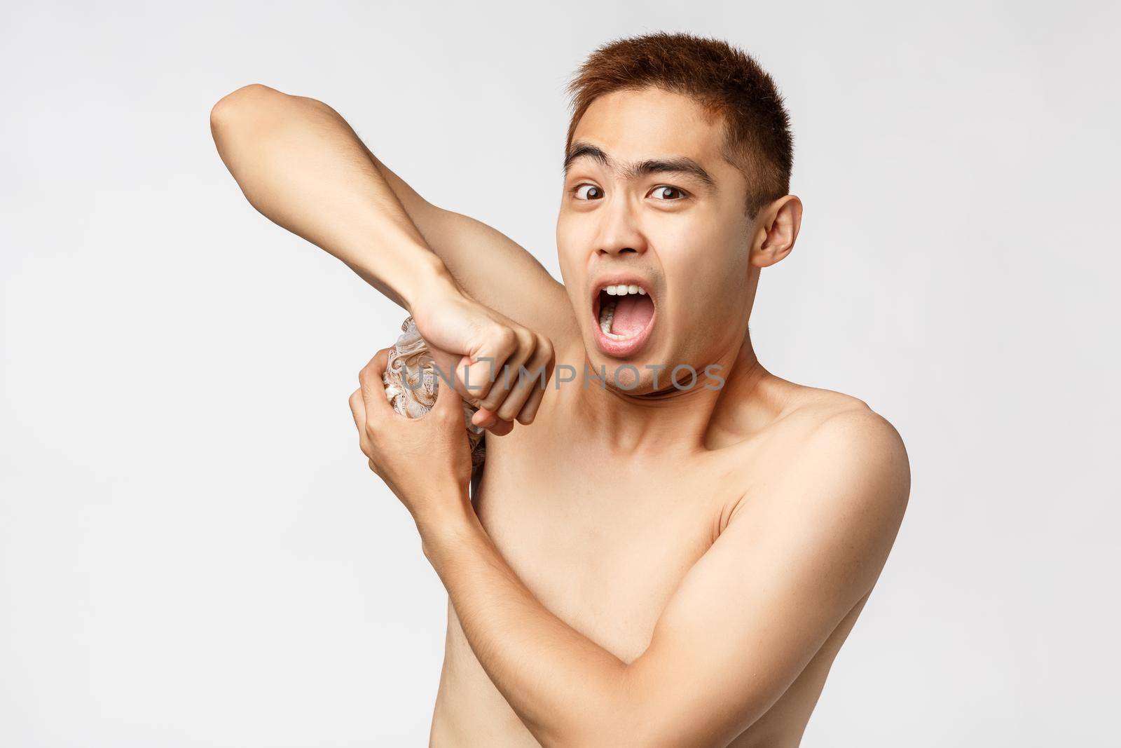 Beauty, people and hygiene concept. Portrait of shocked funny asian naked man, watching armpit and being interrupted, someone enter bathroom, standing startled white background.