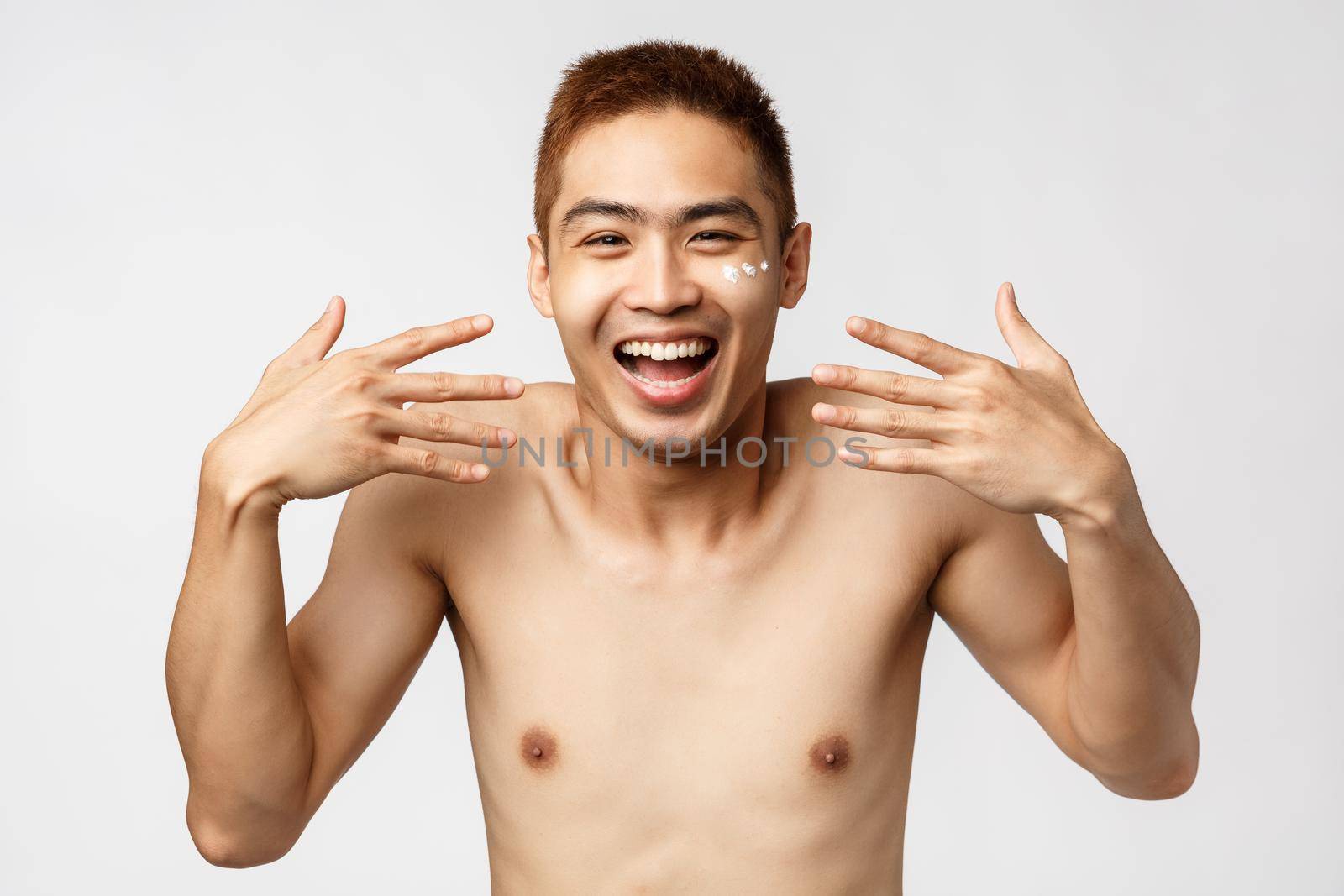 Beauty, people and leisure concept. Close-up portrait of enthusiastic, amused asian handsome man with bare torso, shaking hands and laughing, smiling upbeat, apply facial cream by Benzoix